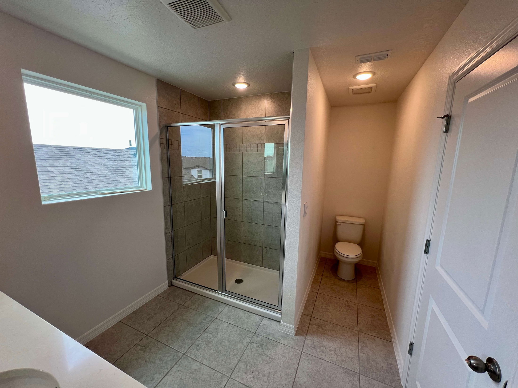 Modern bathroom featuring a glass-enclosed shower and toilet with natural light from a window.