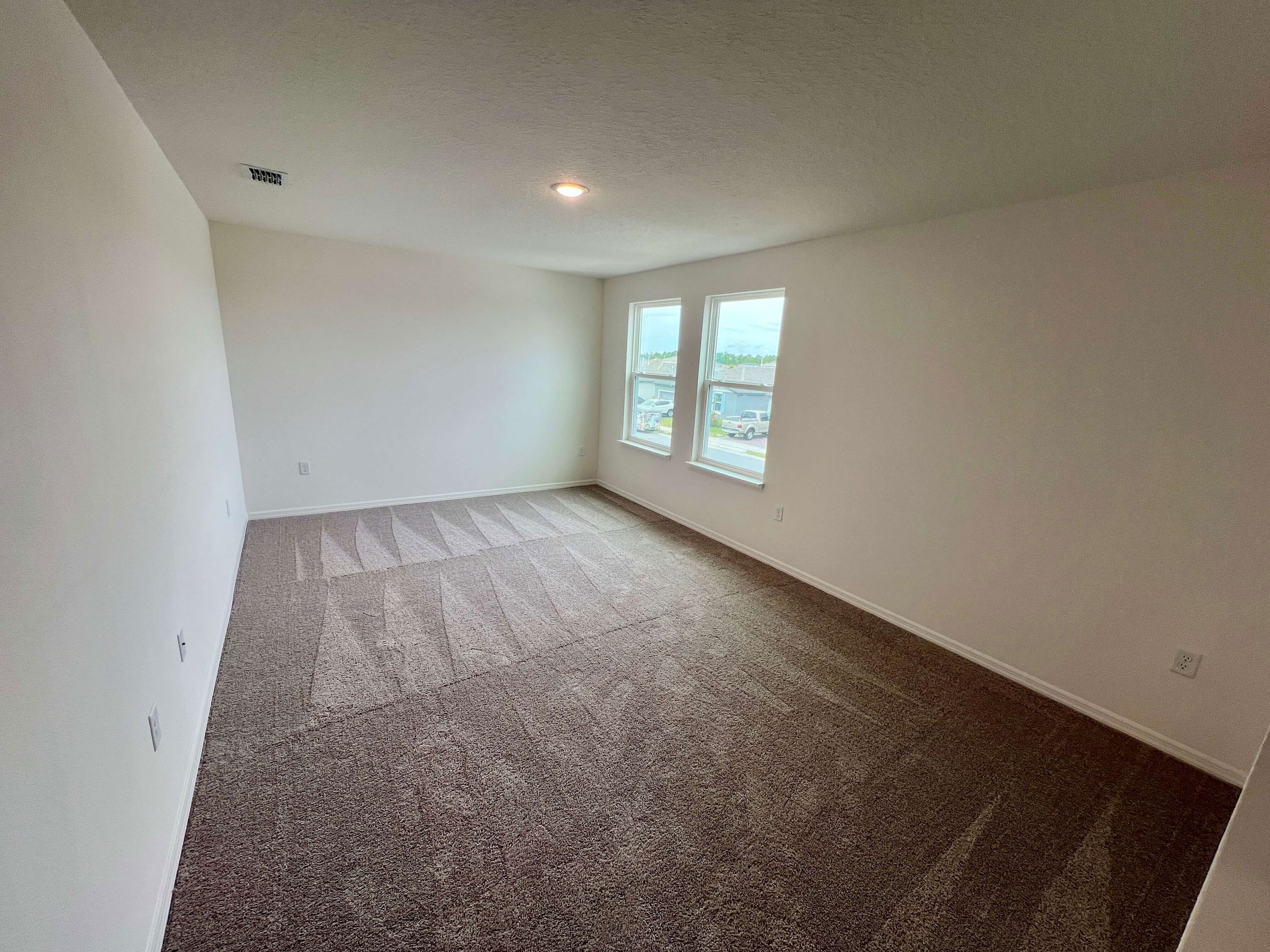 Bright, empty room with clean beige carpet and two large windows.