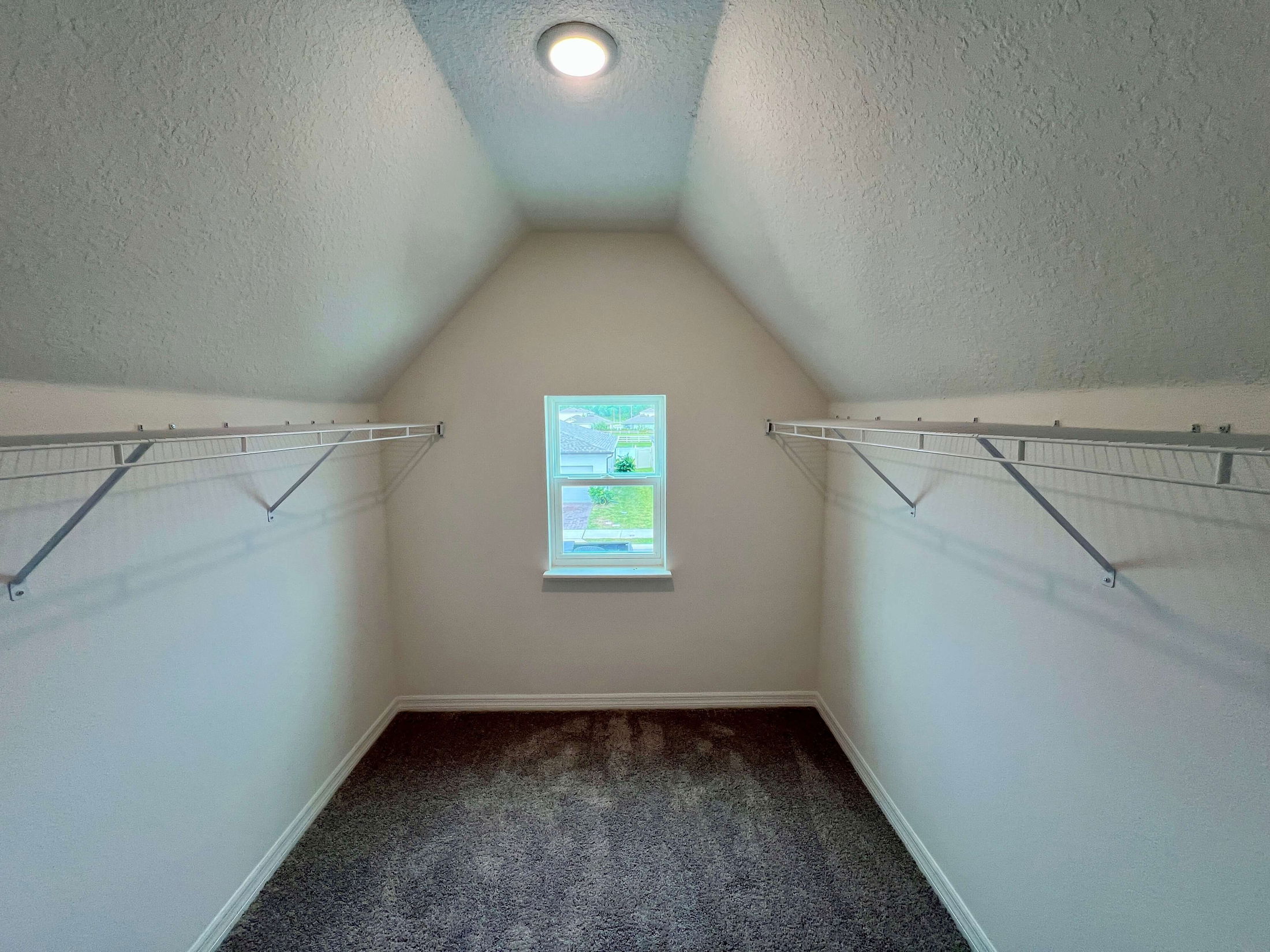 Spacious walk-in closet with high ceiling, featuring white wire shelving and natural light from a small window.