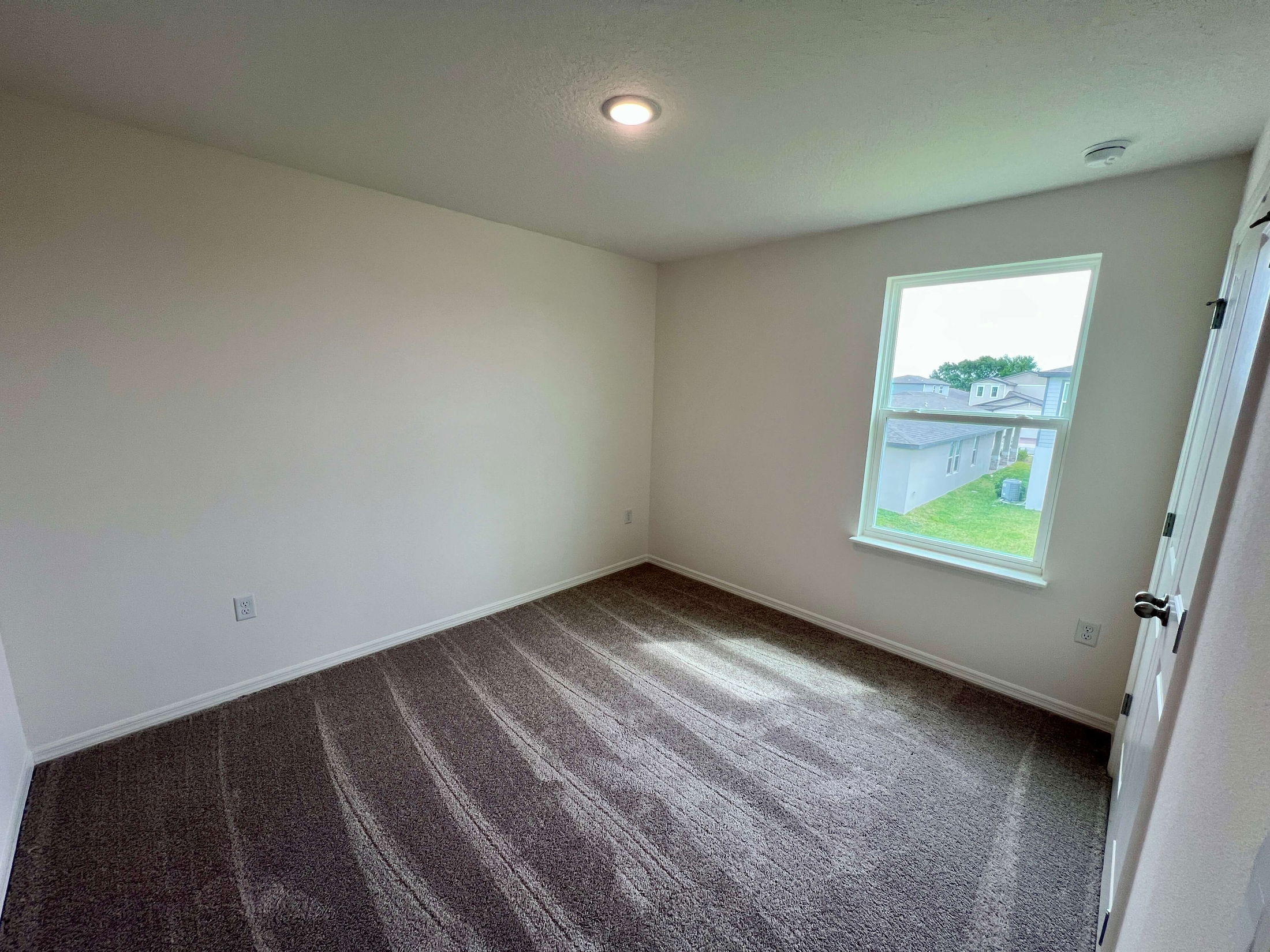 Empty carpeted room with white walls, a single window, and a ceiling light, ideal for a small bedroom setup.