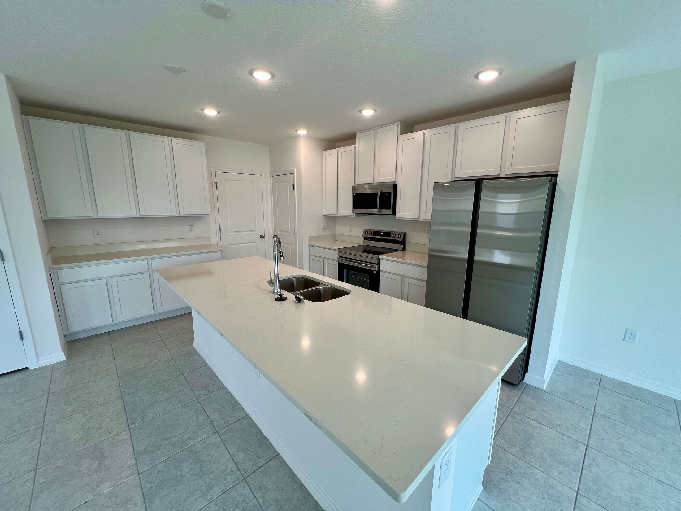 Modern kitchen with white cabinets, stainless steel appliances, and a large central island featuring a double sink under recessed lighting.
