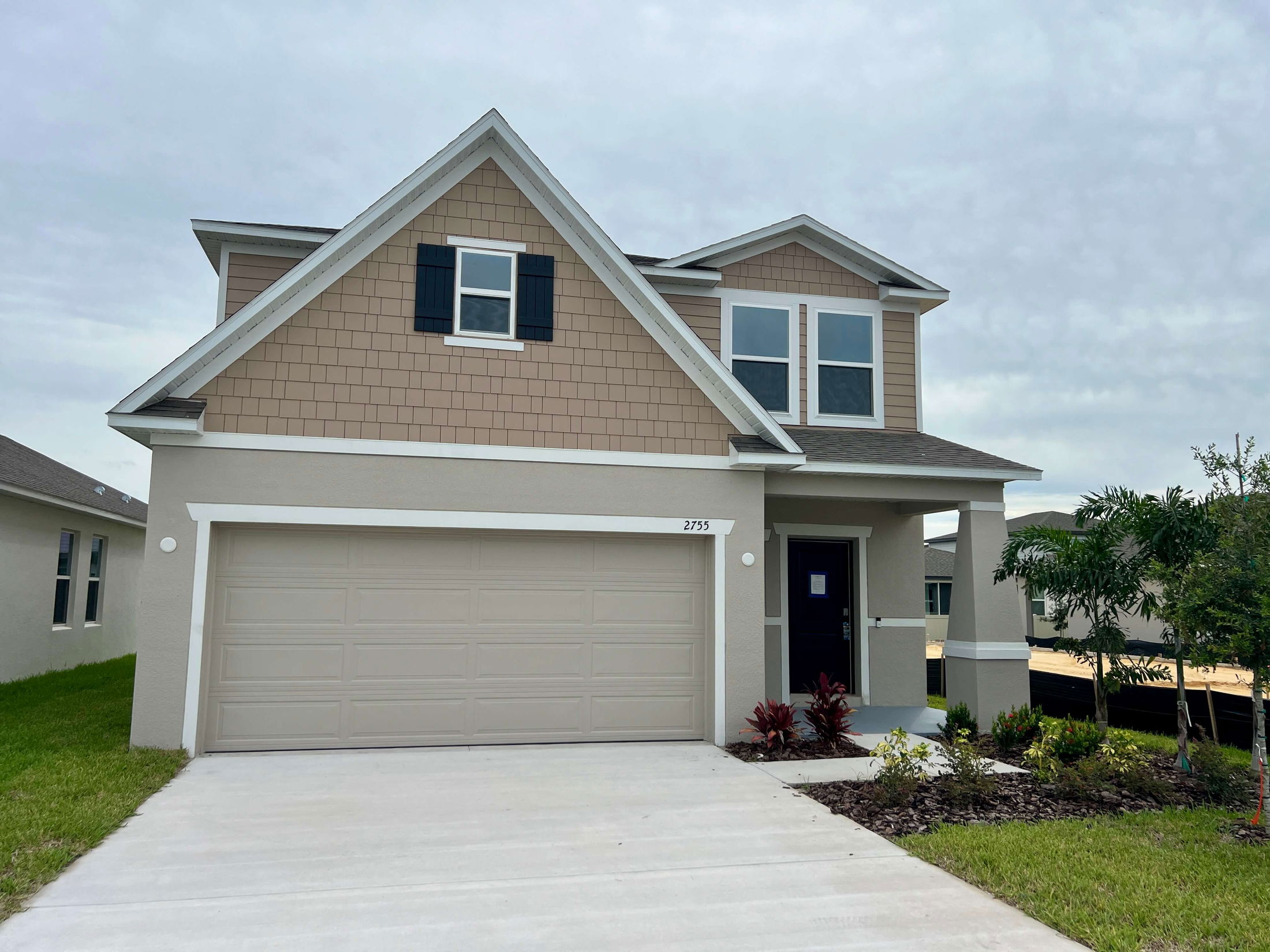 Modern two-story suburban home with beige siding, large garage, and a manicured front lawn.