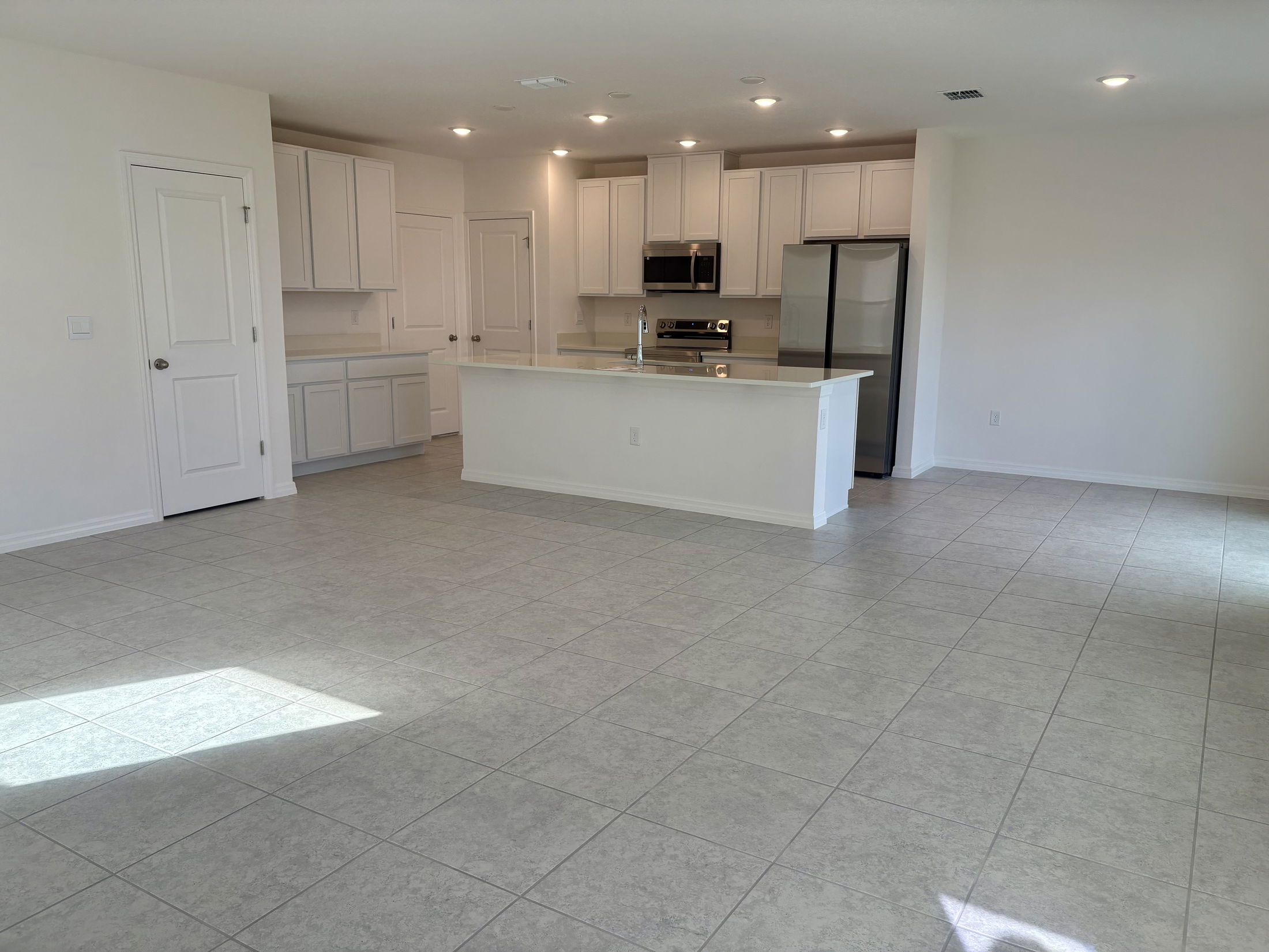 Spacious modern kitchen with white cabinets, stainless steel appliances, and a large open floor plan with tiled flooring.