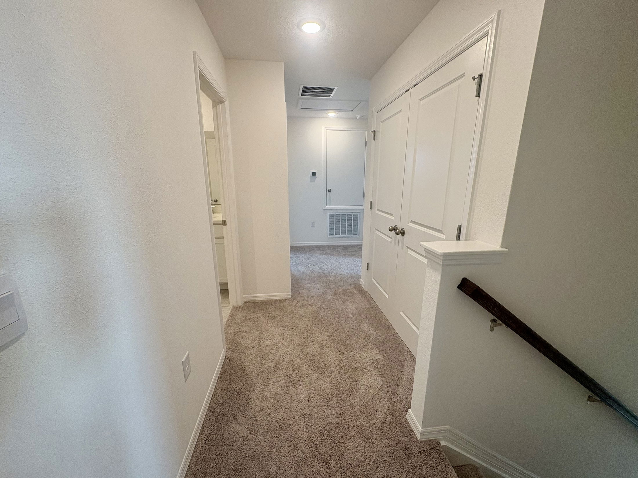 Bright, carpeted hallway in a modern home with white walls and multiple doors.