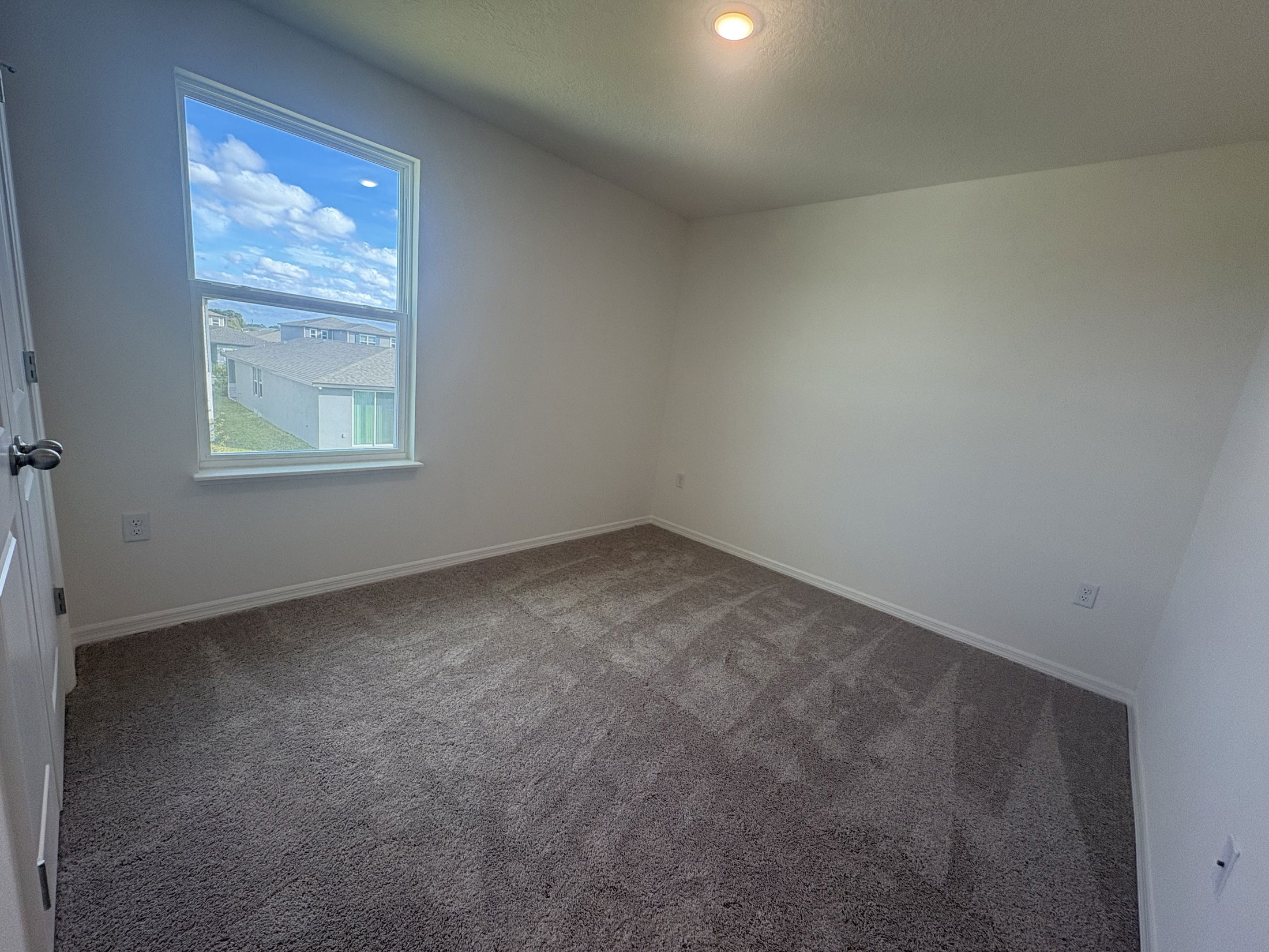 Spacious empty room with beige carpet and a large window showcasing a blue sky view.