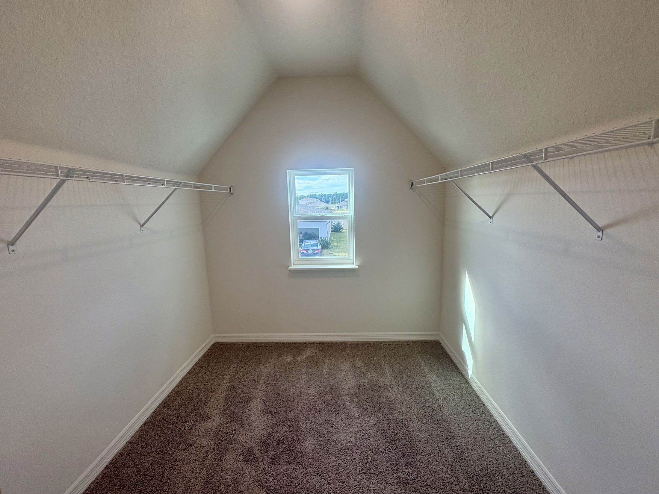 Spacious walk-in closet with carpet and wire shelving on both sides, illuminated by a window with natural light.