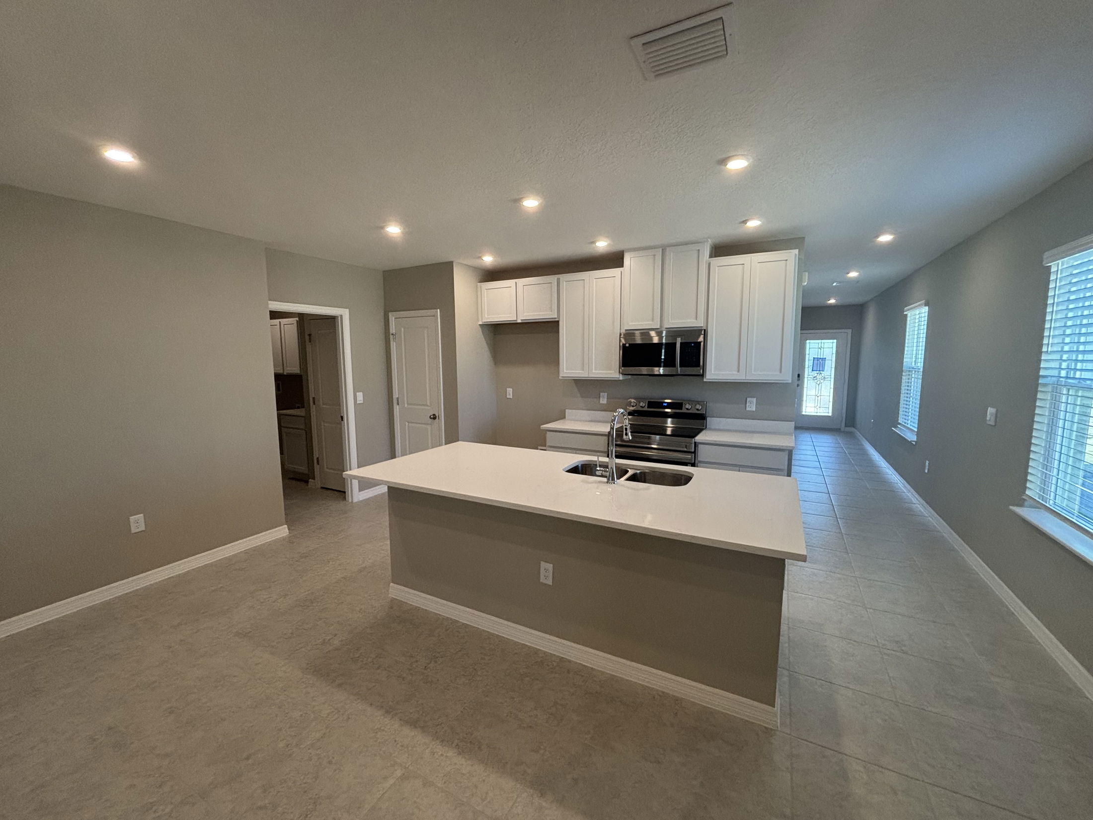 Modern kitchen interior with white cabinets, stainless steel appliances, and a large island in a spacious, open-concept layout.