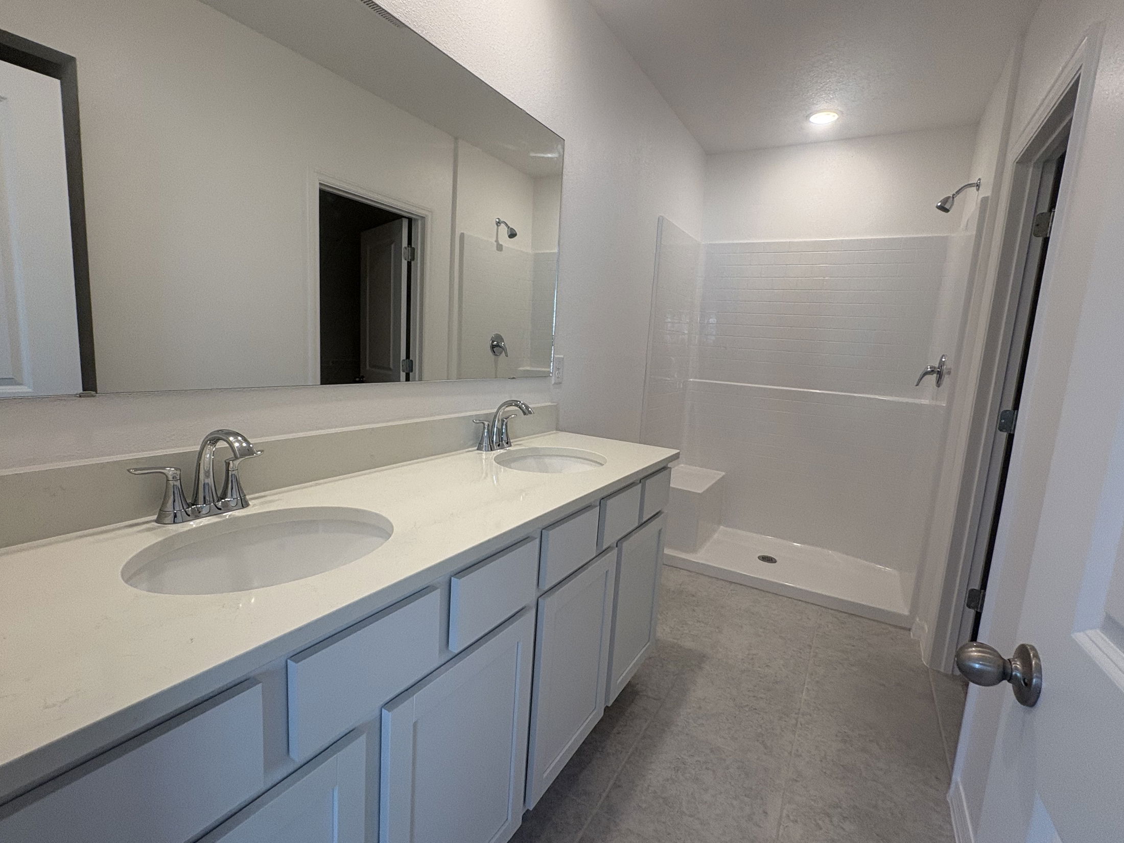 Modern bathroom with a double vanity and glass-enclosed shower featuring white cabinetry and fixtures.