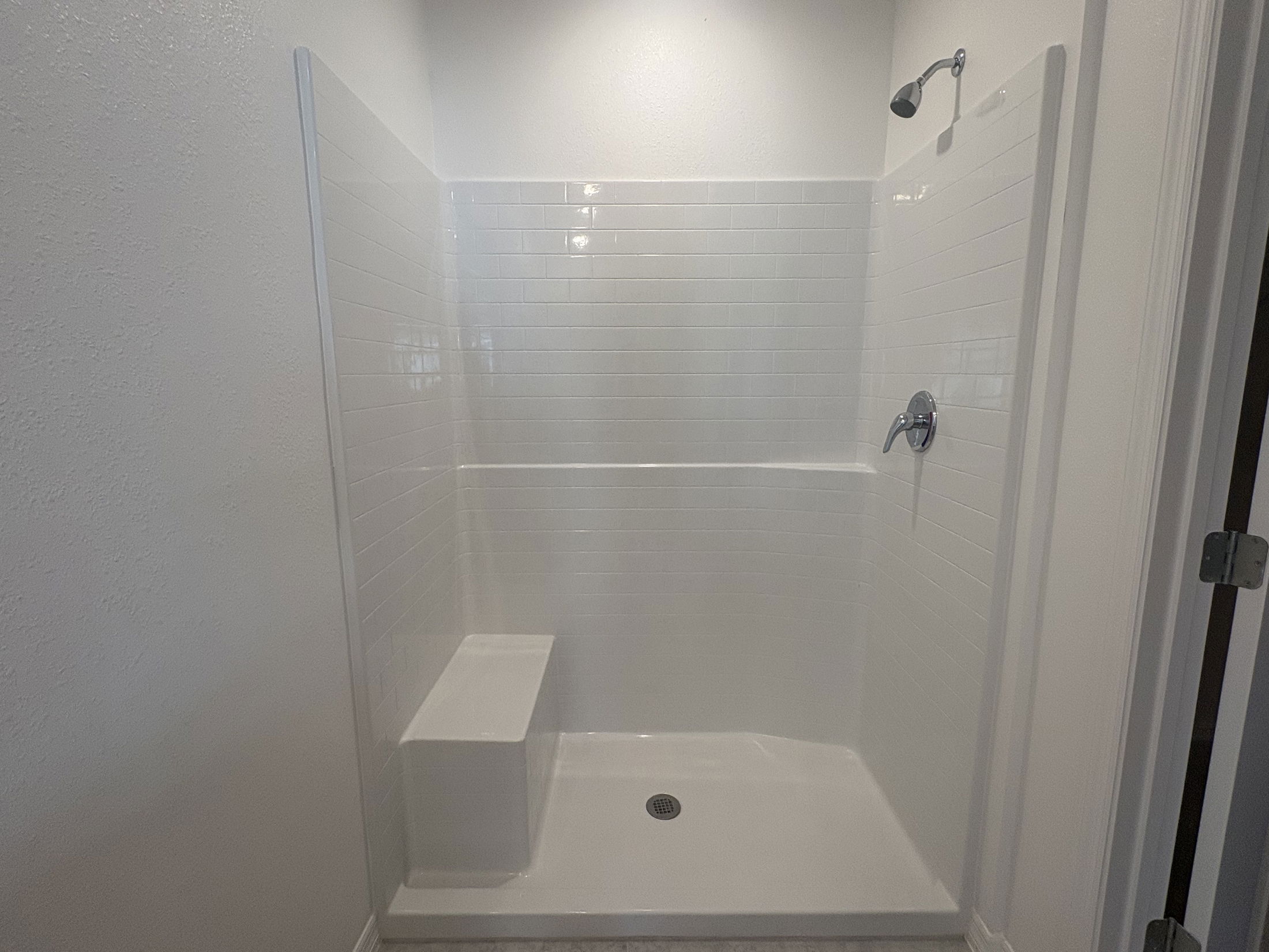 Modern white tiled shower enclosure with built-in bench and stainless steel fixtures.