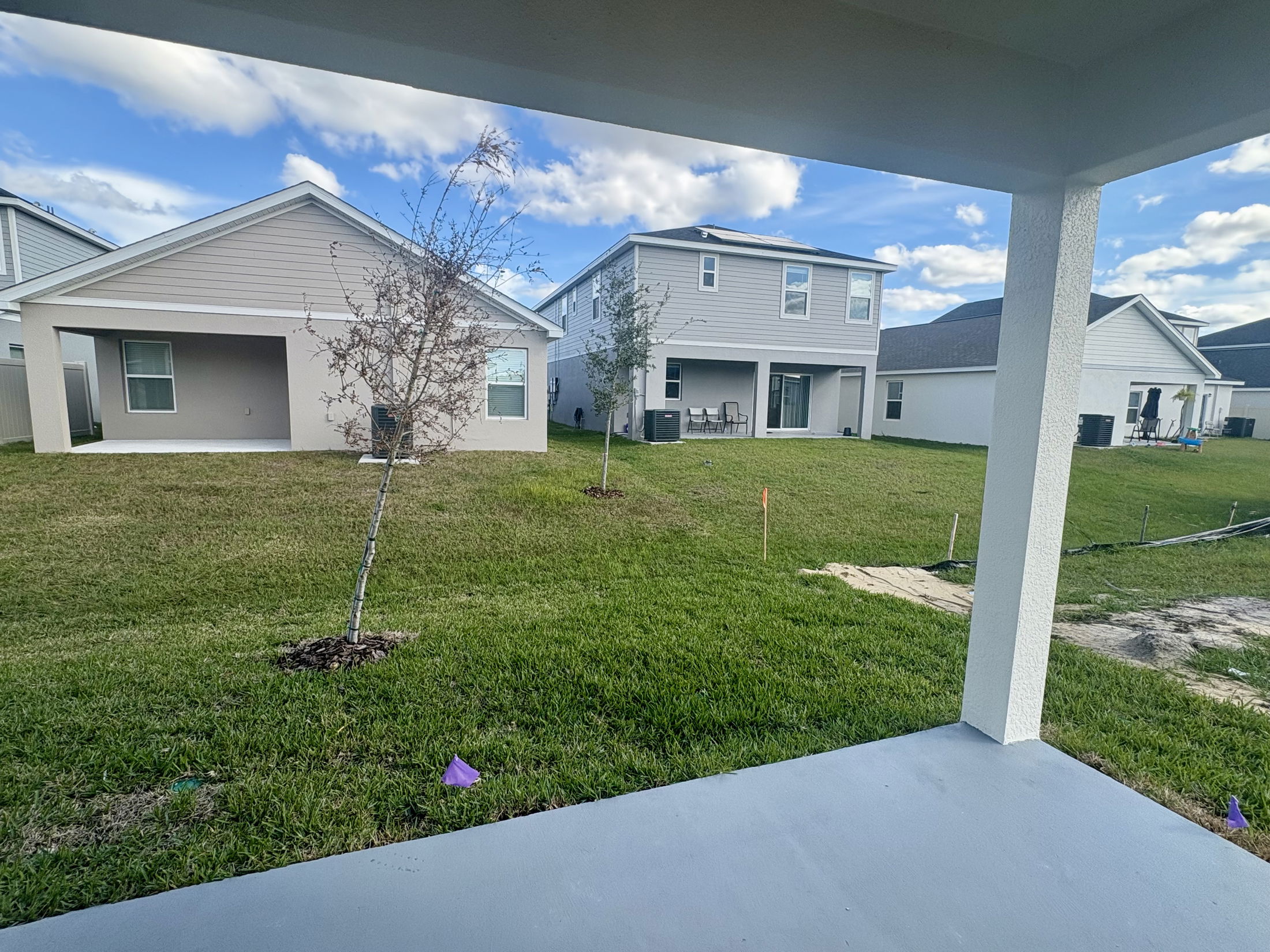 Suburban backyard view with green lawns and modern, two-story houses under a blue sky.