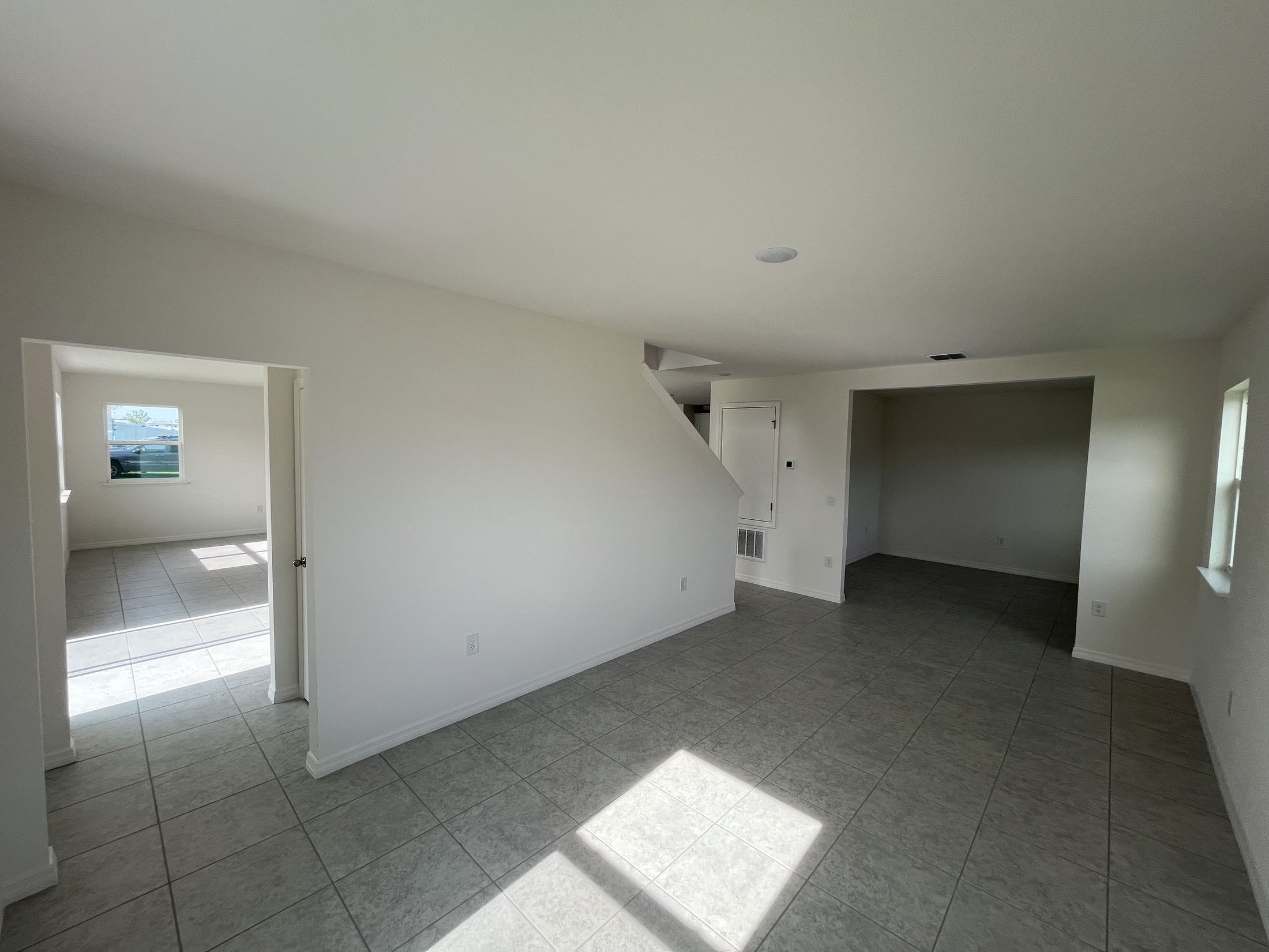 Spacious, sunlit empty room with tiled flooring and white walls in a modern home interior.
