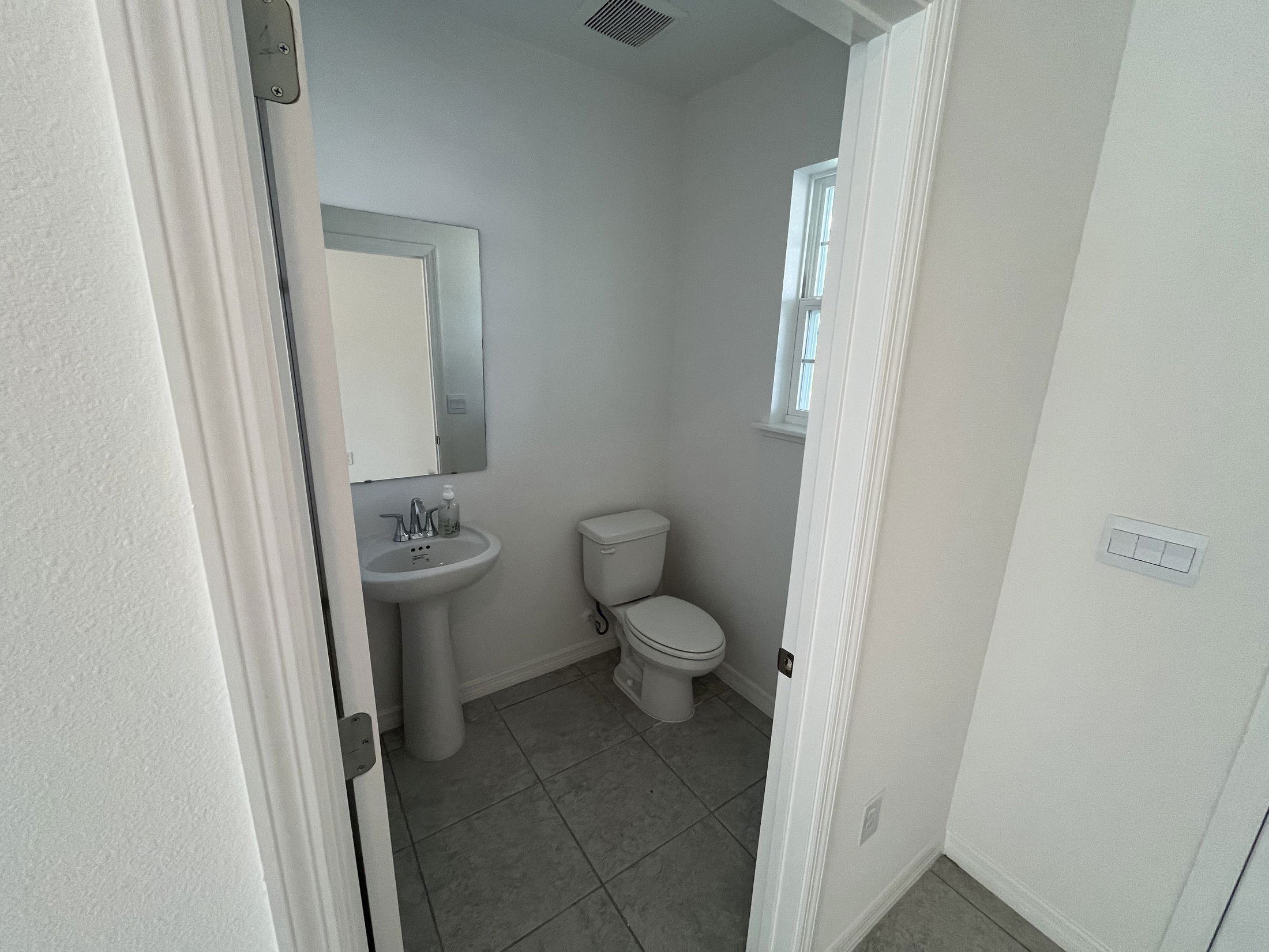 Compact modern bathroom with white pedestal sink, toilet, and gray floor tiles.