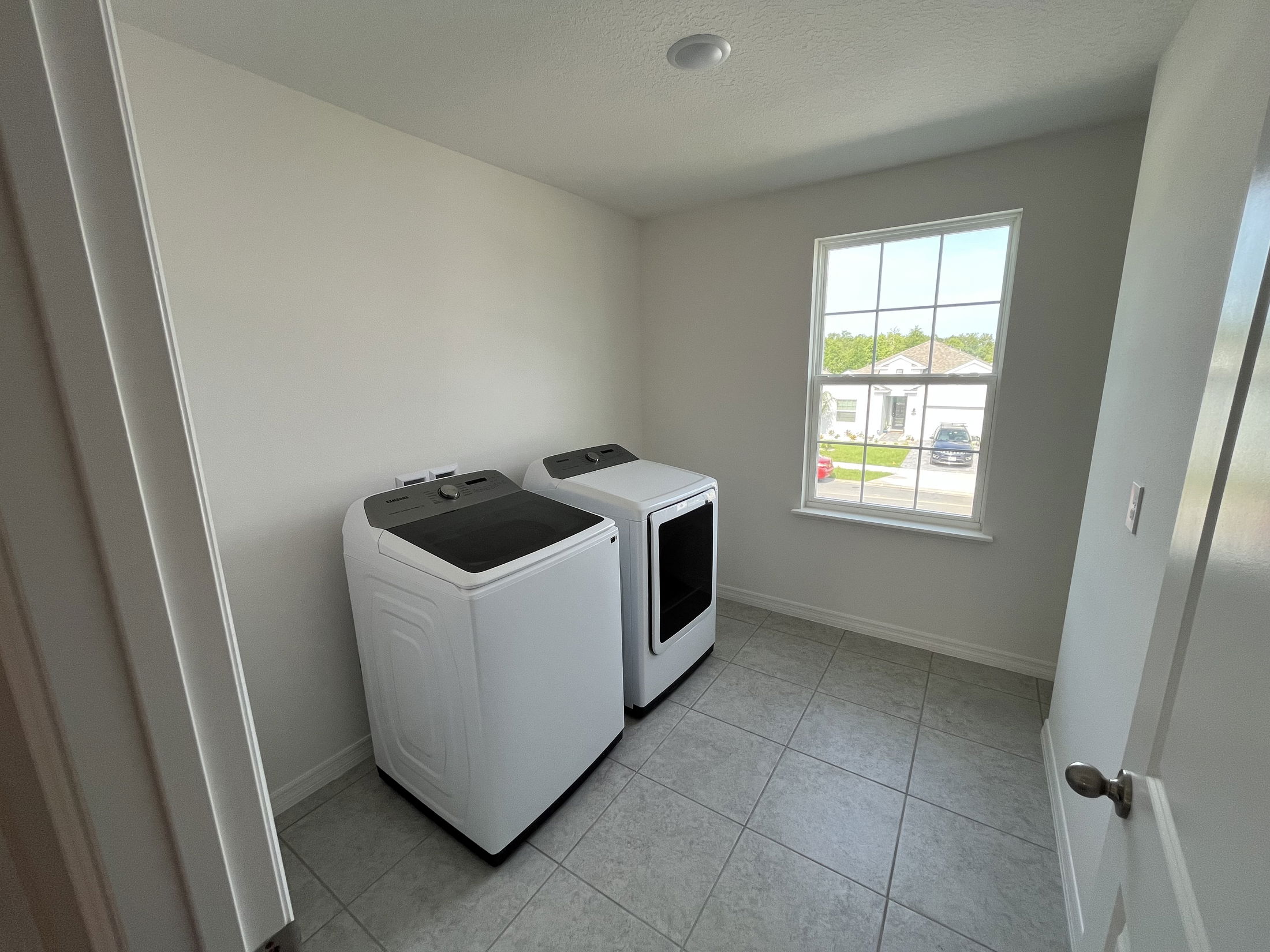 Laundry room with modern washer and dryer next to a window, featuring tiled flooring and neutral walls.