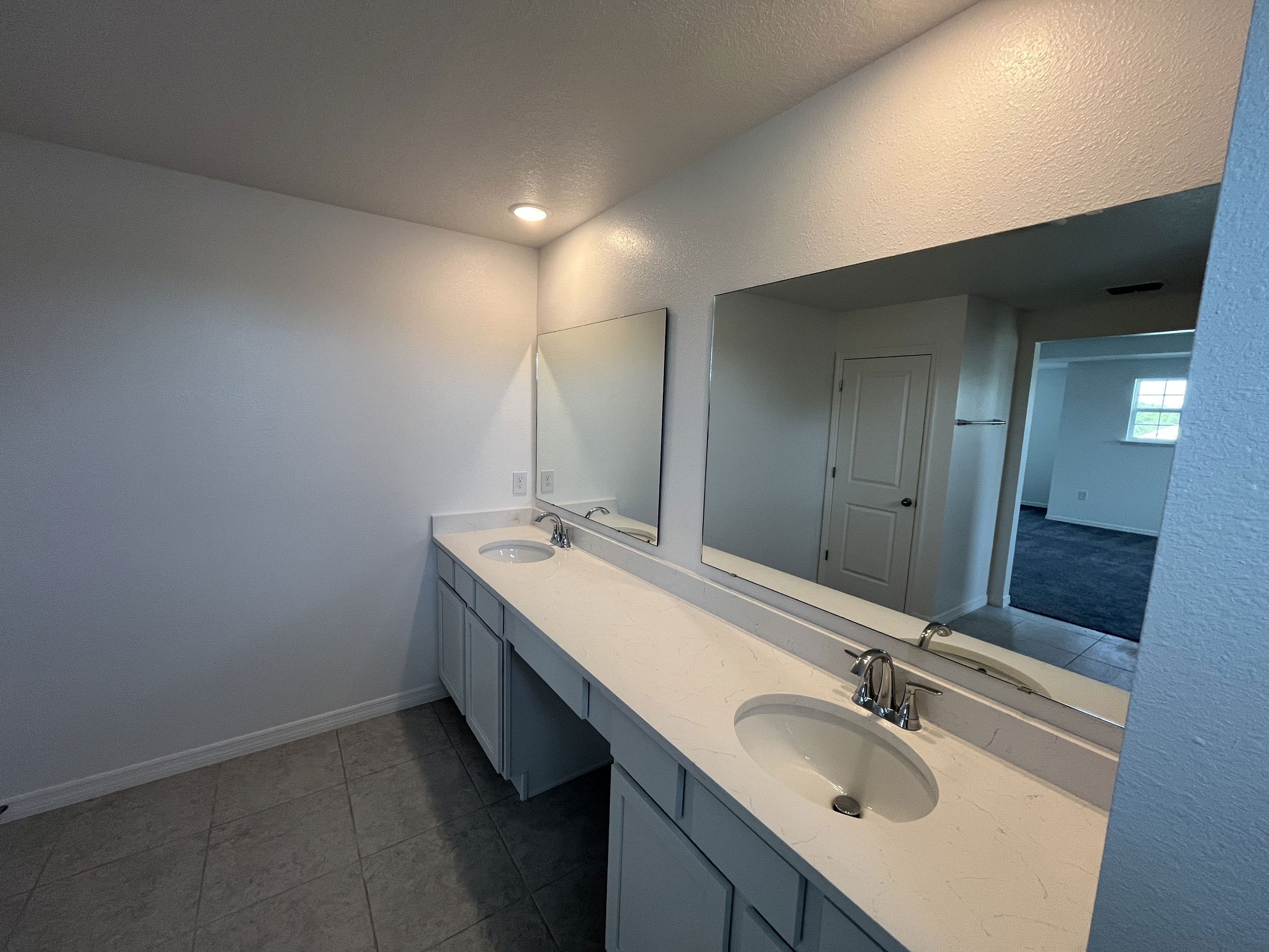 Modern bathroom vanity with dual sinks, large mirrors, and white countertops in a brightly lit room.