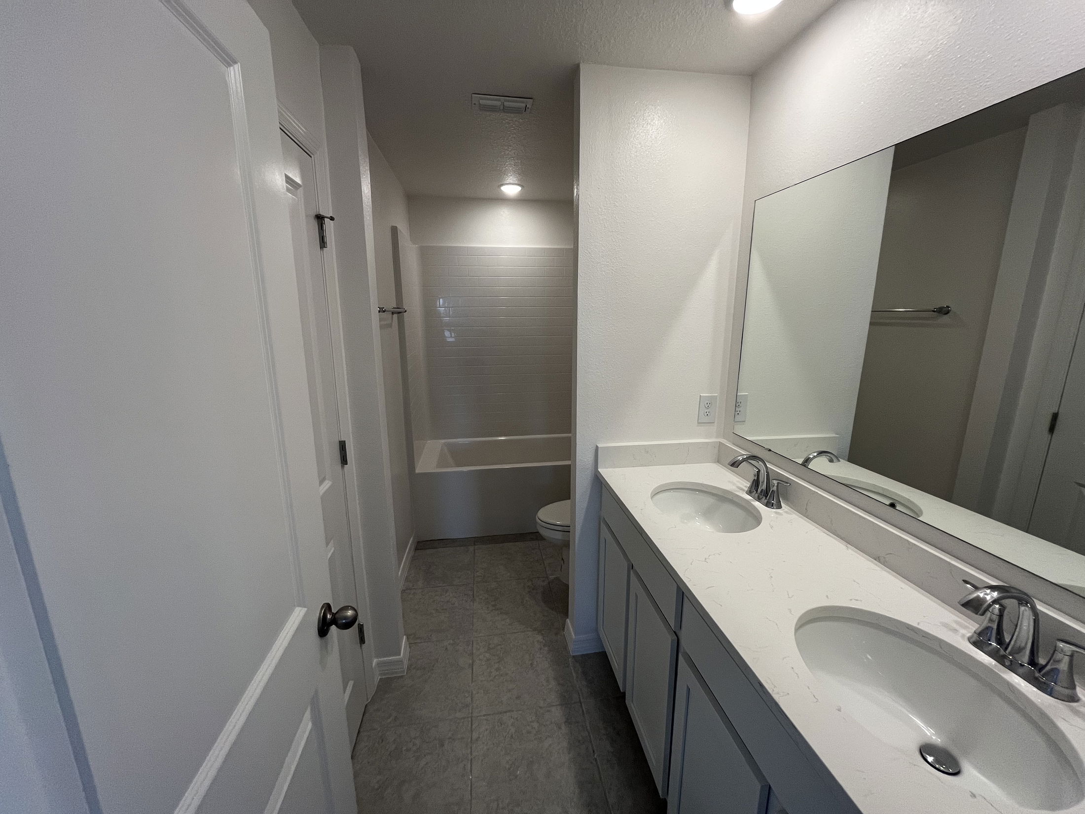 Modern bathroom featuring a dual-sink vanity, large mirror, and a bathtub with a white tiled wall.
