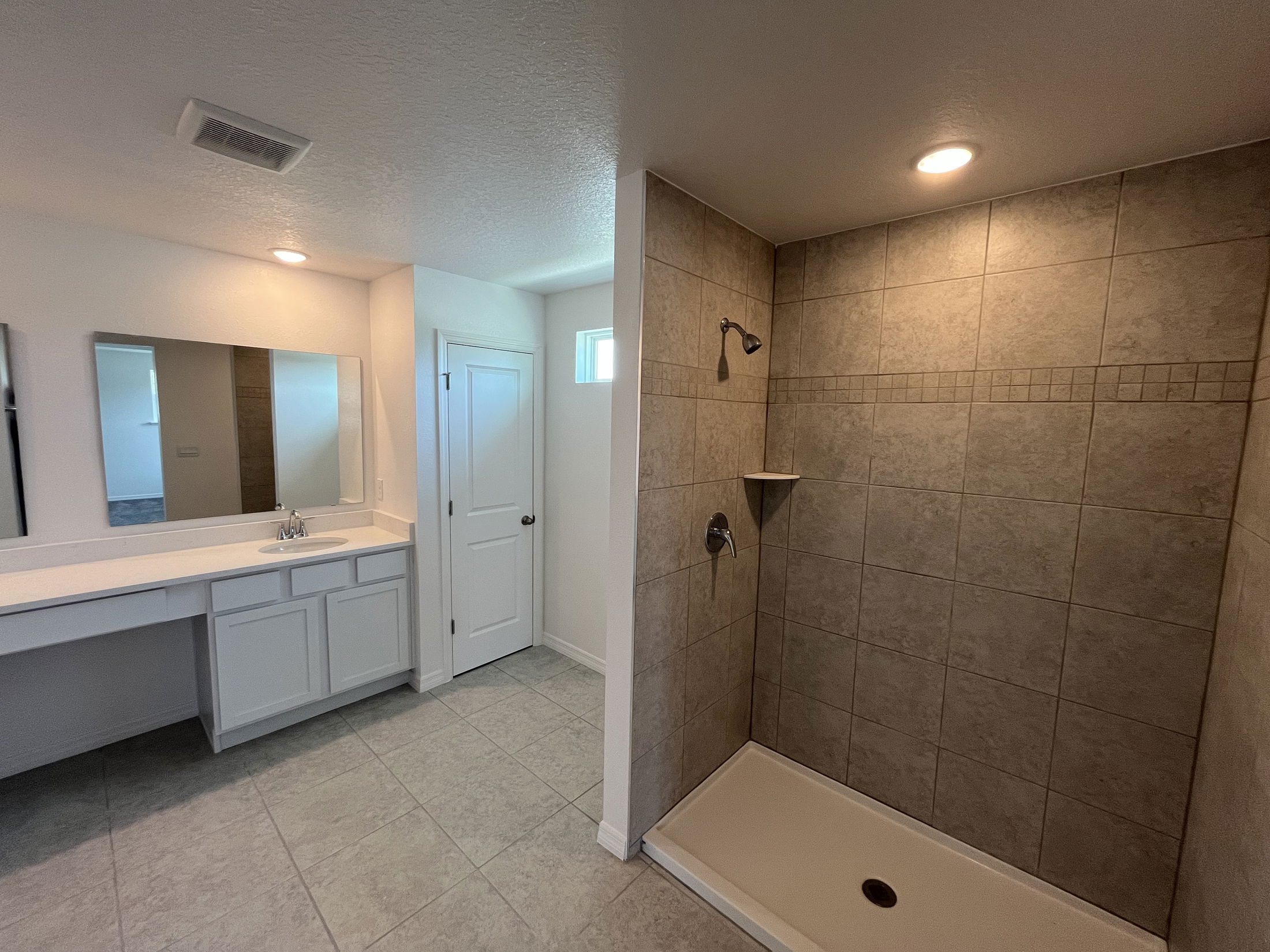 Modern bathroom featuring a spacious walk-in shower with beige tiles and a wide vanity with a mirror and single sink.