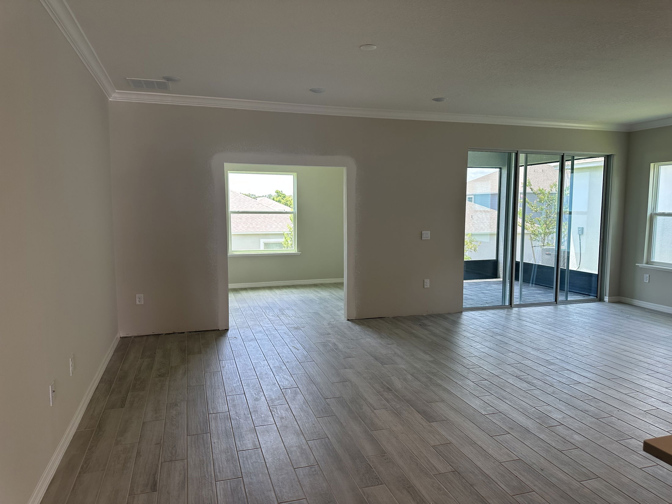 Modern empty living room with wood-style tile flooring, large windows, and a sliding glass door leading to a balcony.