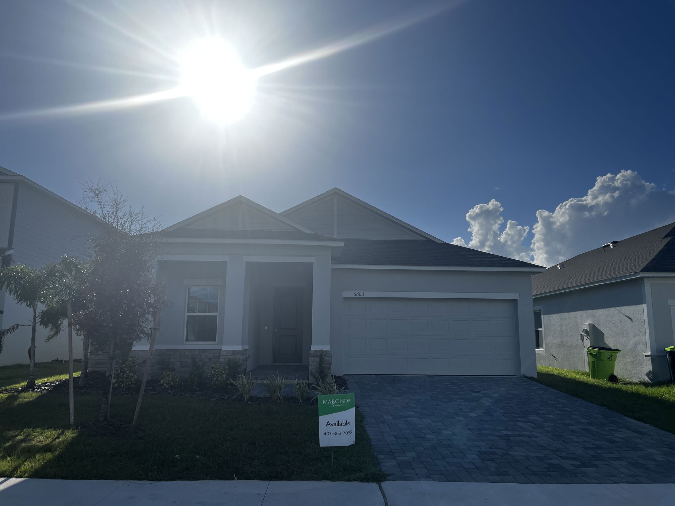 Front view of a modern single-story house with a two-car garage under a bright sunlit sky.