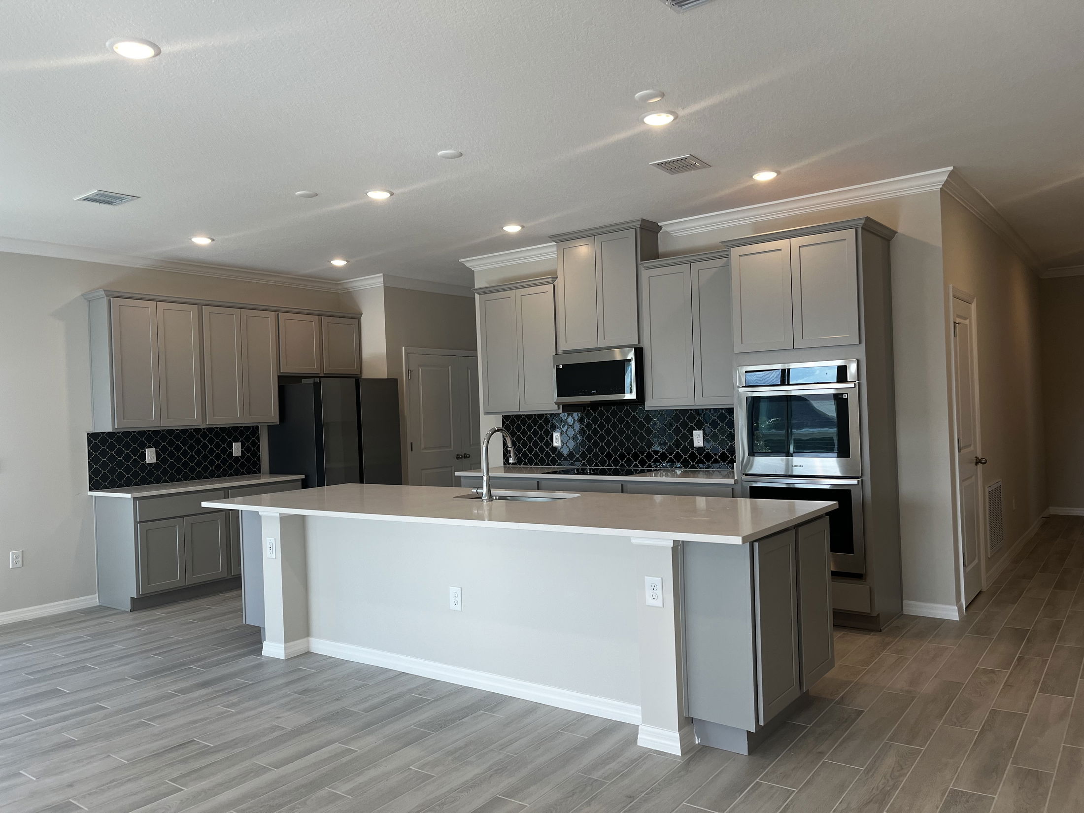 Modern kitchen interior with light gray cabinetry, island, stainless steel appliances, and dark backsplash.