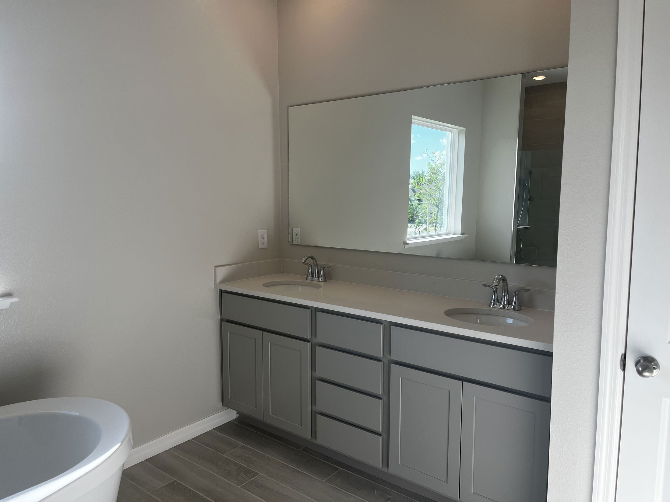 Modern bathroom with double sinks, large mirror, gray cabinetry, and natural lighting from a window.