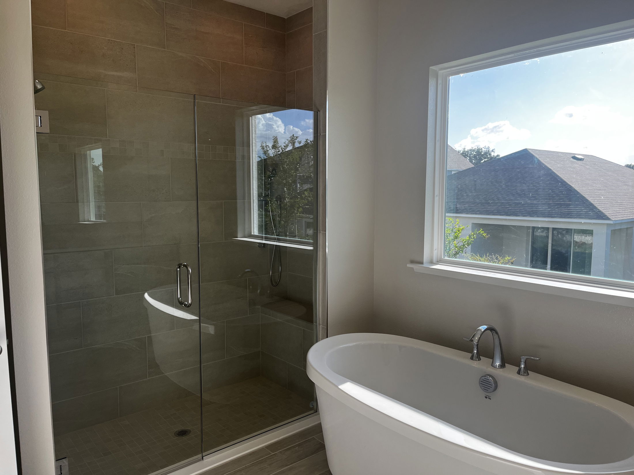 Modern bathroom with a glass-enclosed shower and a freestanding bathtub next to a large window.
