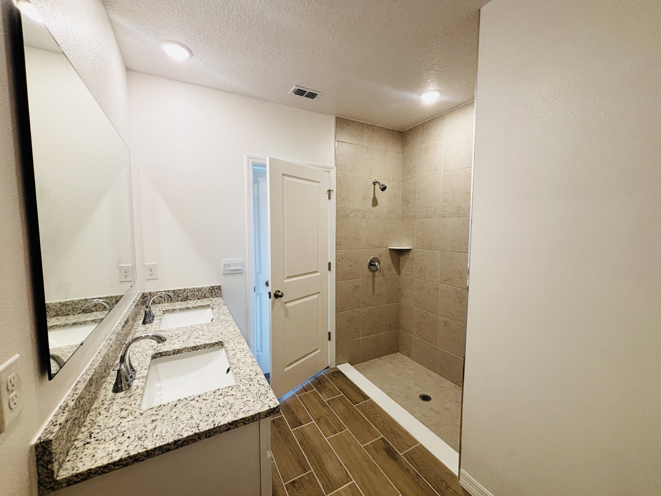 Modern bathroom featuring a double sink vanity, a large mirror, and a walk-in shower with stone tiles.