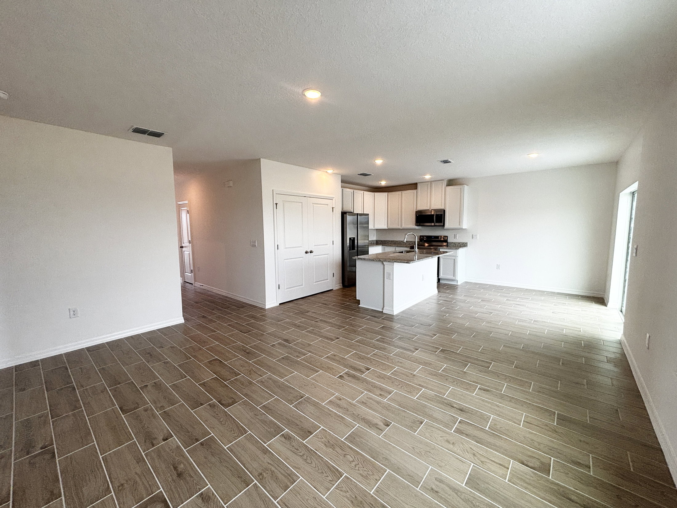 Spacious, empty living area with tiled flooring and a light-filled kitchen area.