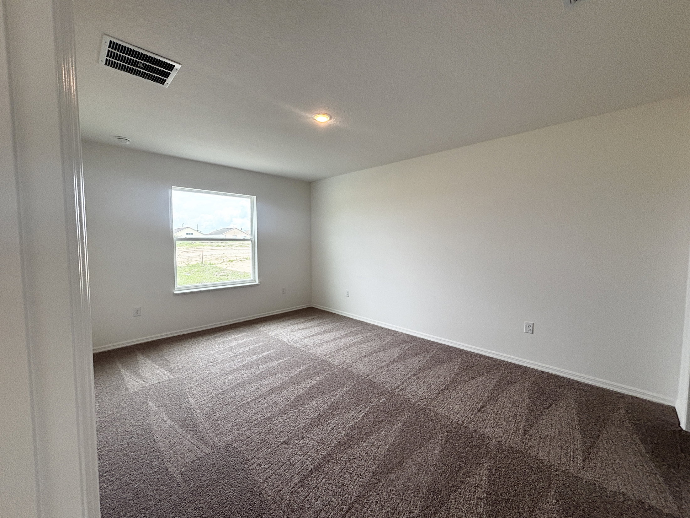 A spacious, empty room with beige carpet and a window overlooking a field.