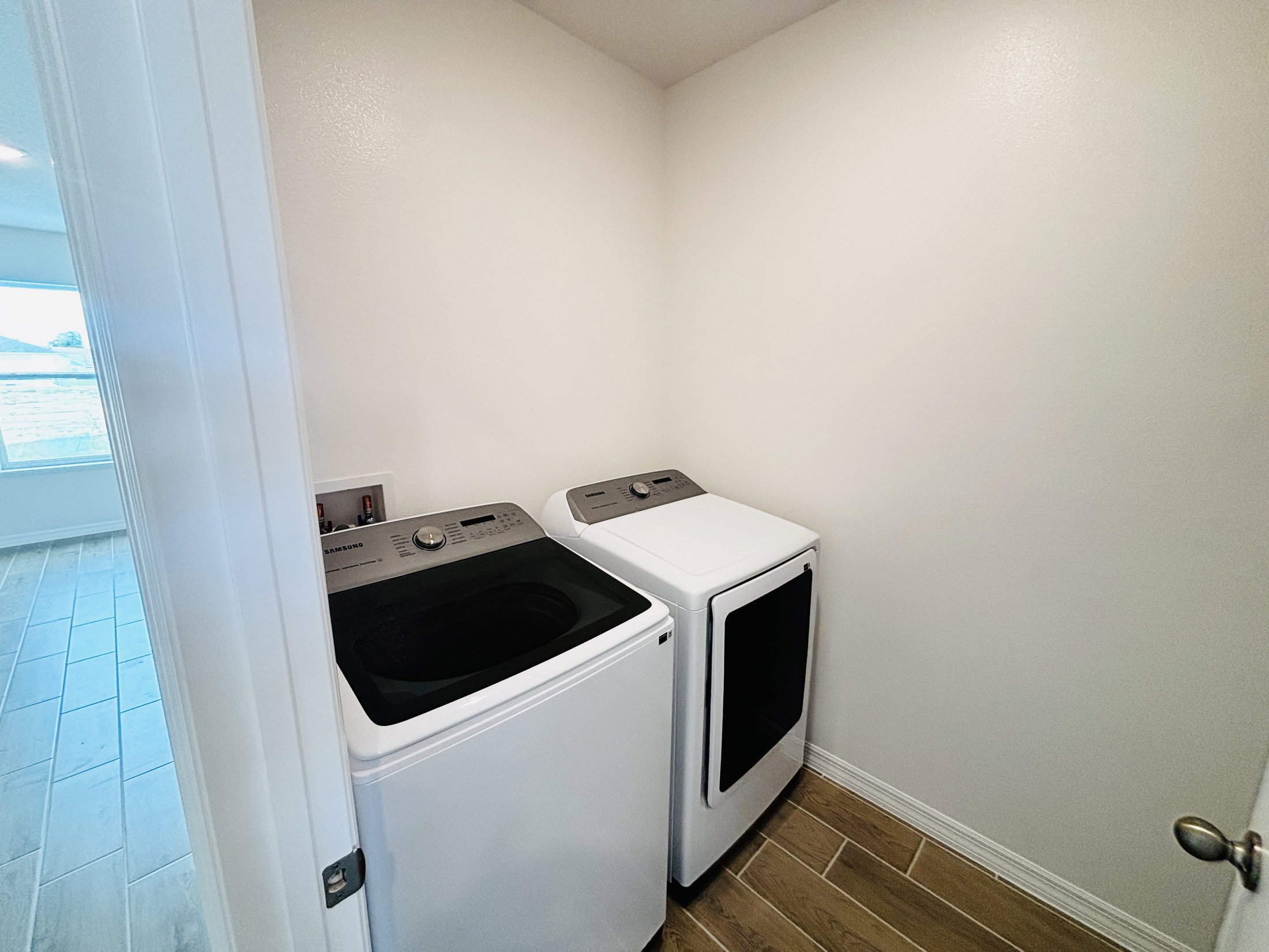 A white washing machine and dryer are placed side by side in a small, brightly lit laundry room.
