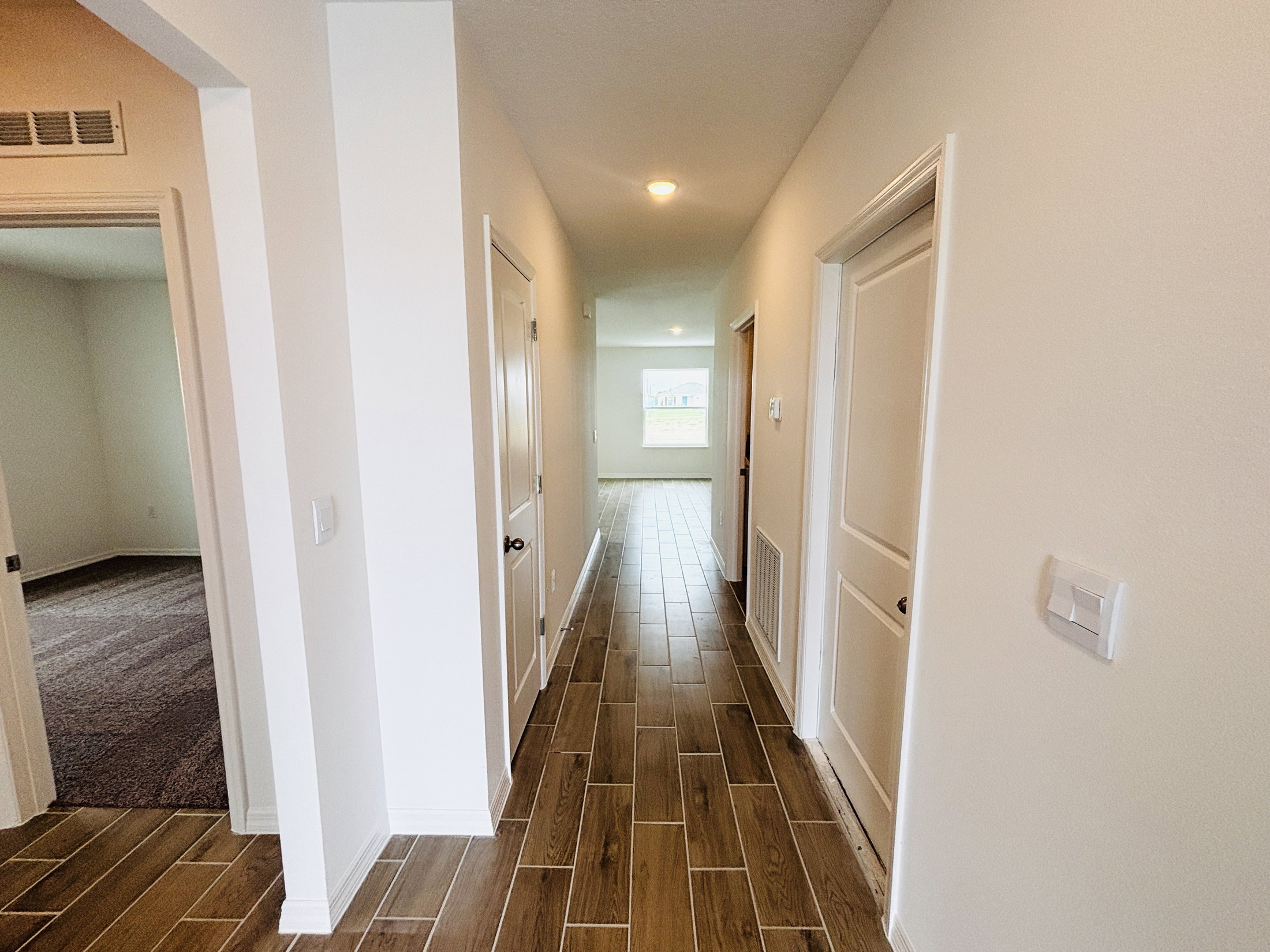 A hallway with white walls and tiled flooring leads to an open area with natural light.