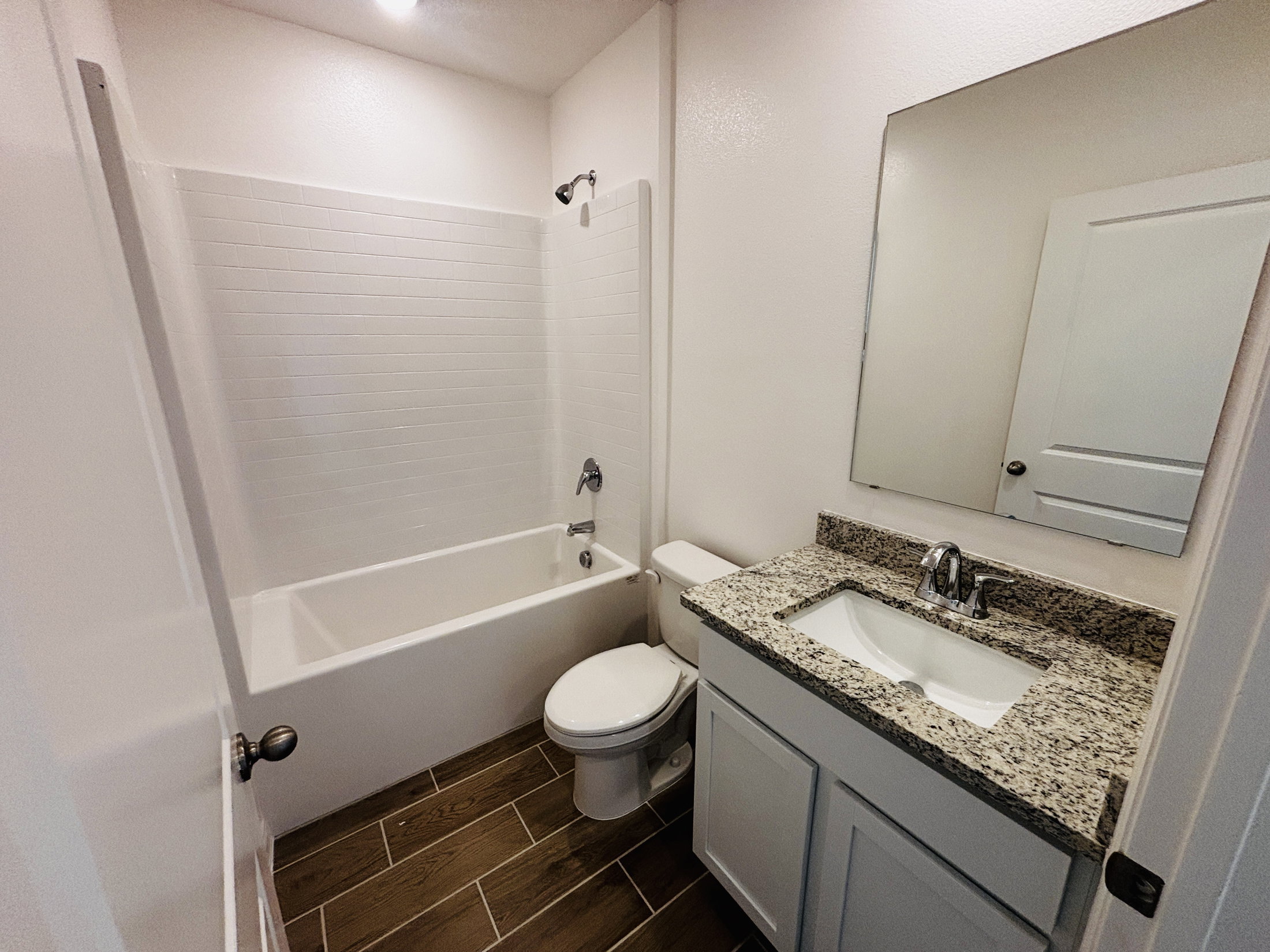 A small bathroom with a bathtub, toilet, and a sink with a granite countertop.