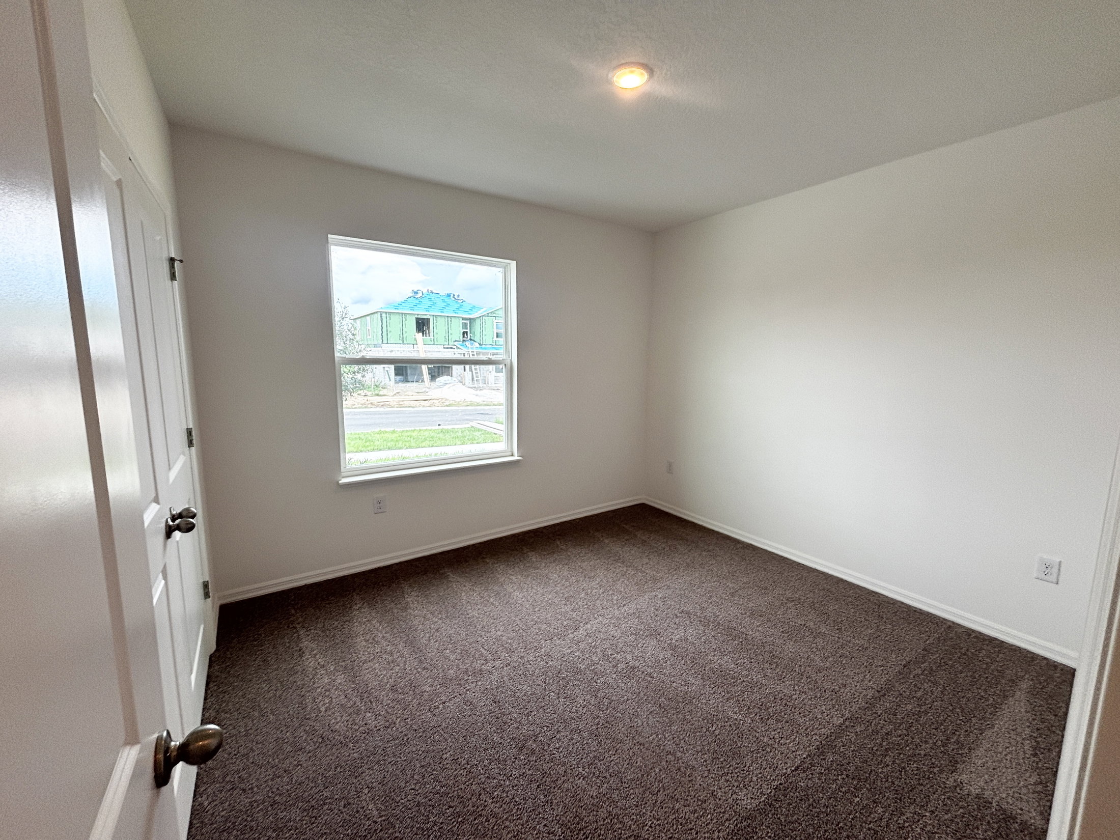 A vacant room with beige carpet, white walls, and a window showcasing a construction site outside.