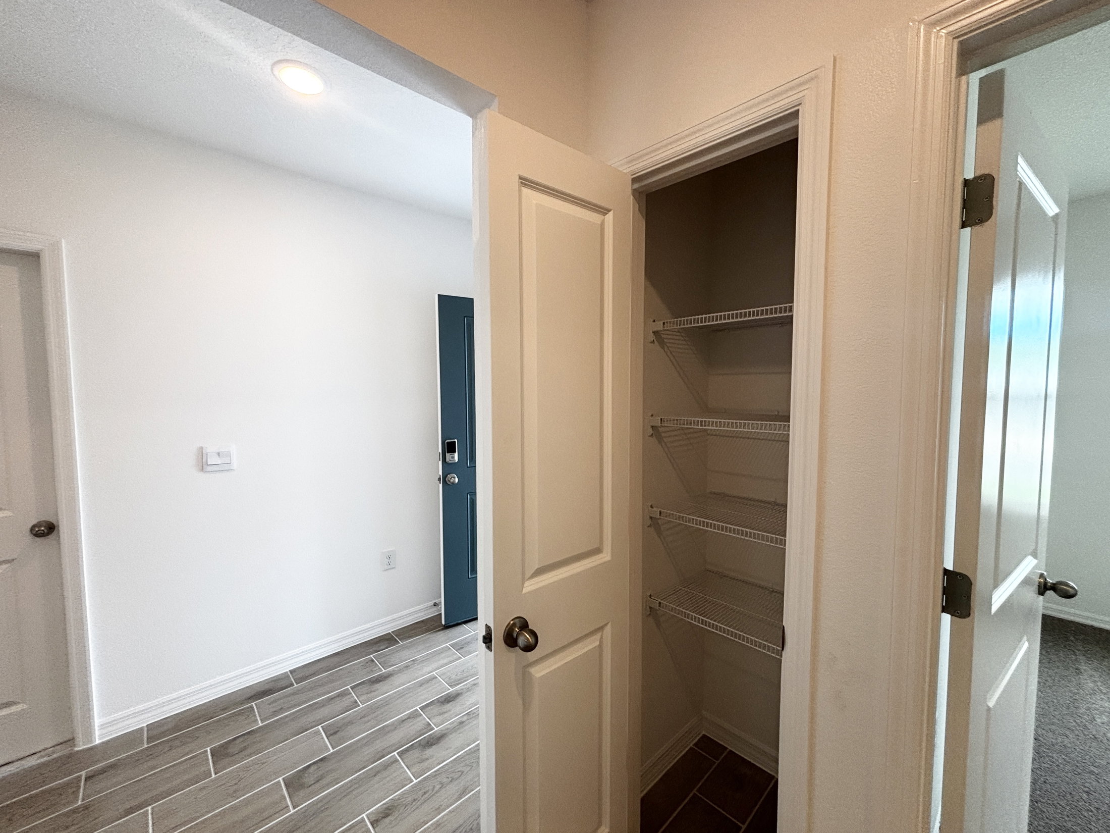 An open closet with wire shelving in a hallway next to a door leading to another room.
