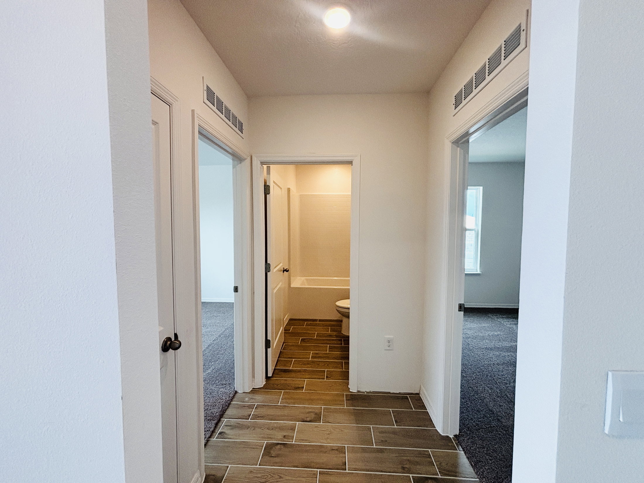 A hallway with three open doors leading to different rooms, featuring tile flooring and neutral-colored walls.