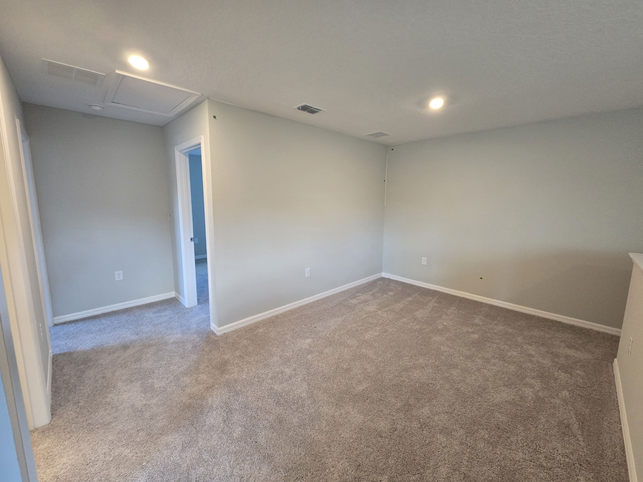 Empty carpeted room with beige walls, recessed lighting, and open doorways.