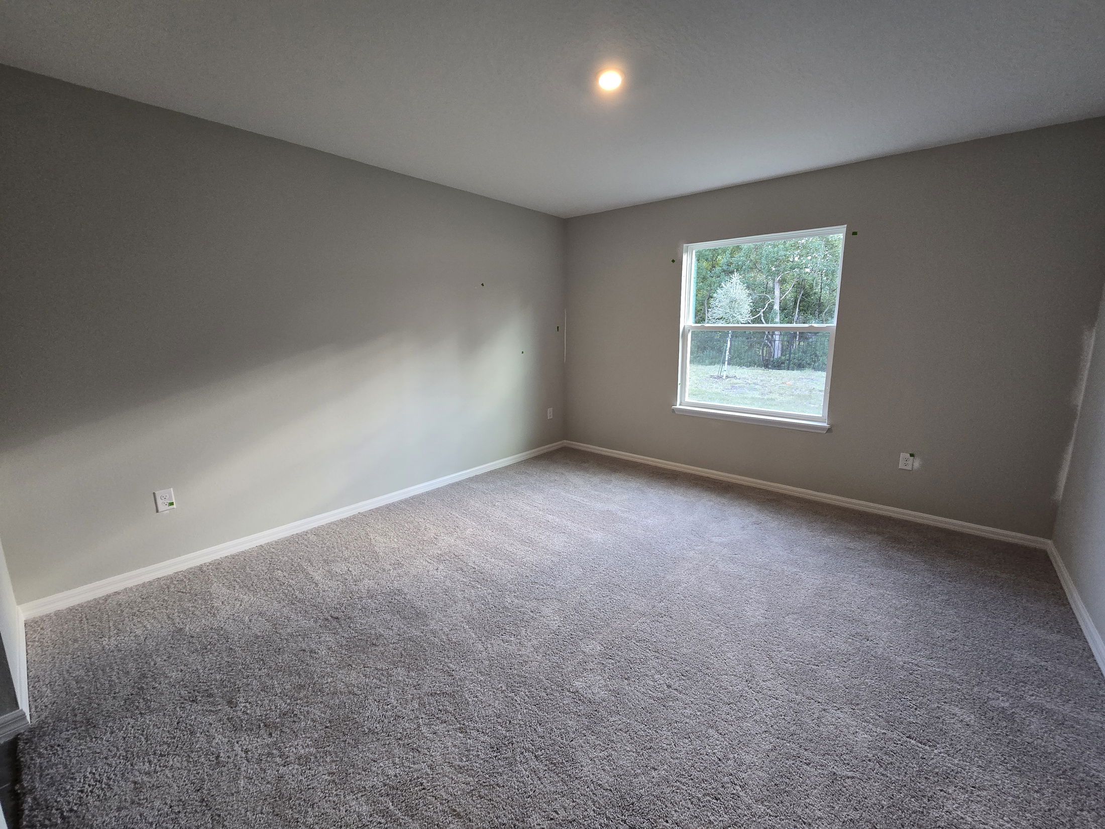 Spacious empty room with gray carpet, a single window, and soft overhead lighting.