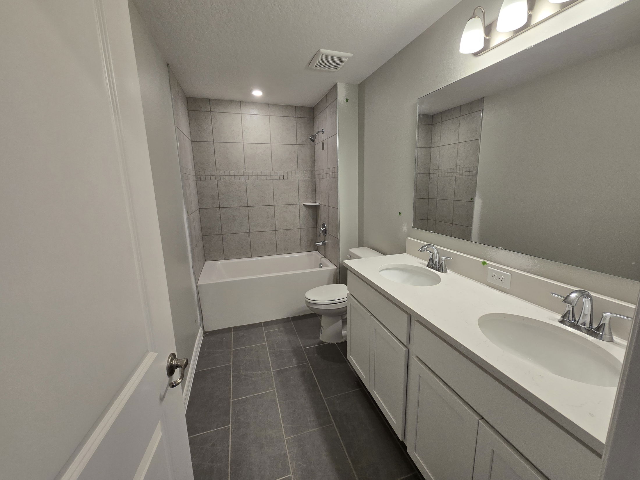 Modern bathroom with dual sinks, white countertops, and a tiled shower-bathtub combination.