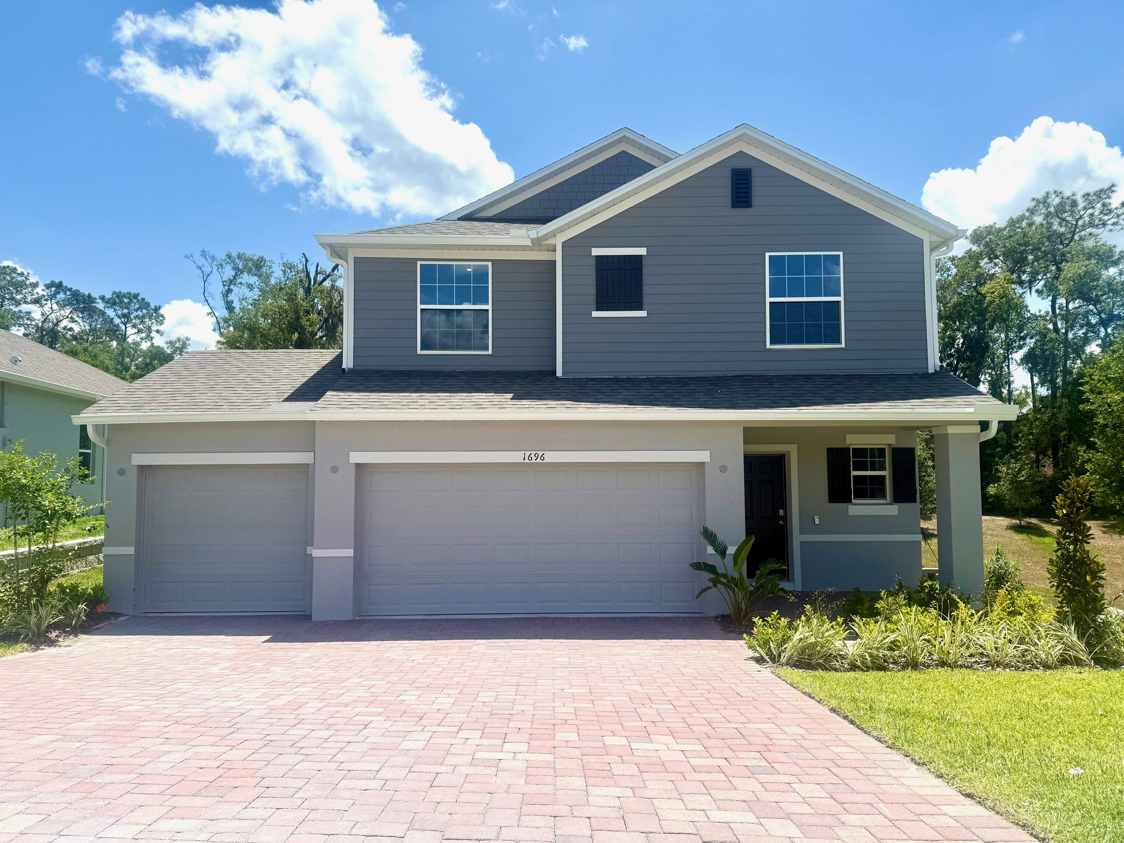 Two-story modern gray house with three-car garage and landscaped front yard under a clear blue sky.