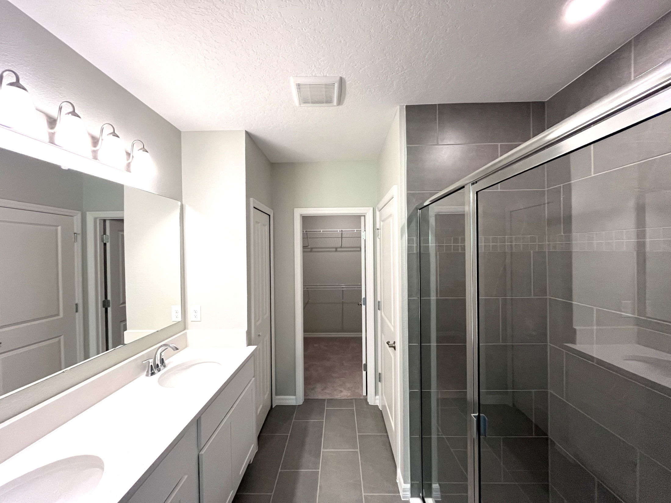 Modern bathroom interior with dual sinks, large mirror, glass shower, and entrance to a walk-in closet.