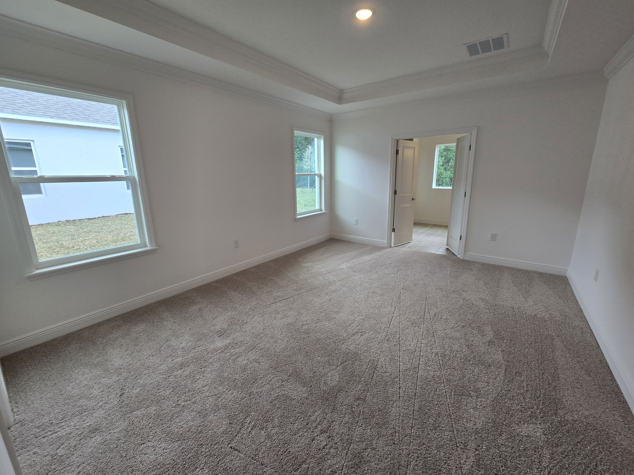 Spacious, carpeted empty bedroom with white walls, two windows, and an open doorway leading to an adjacent room.