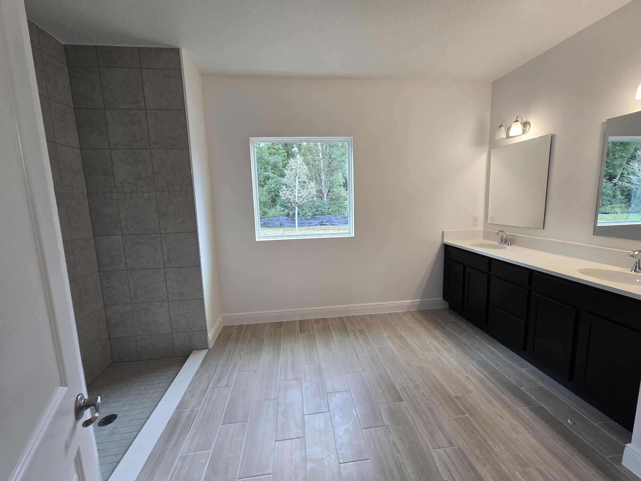 Modern bathroom with a spacious shower, dual-sink vanity, and large window overlooking greenery.