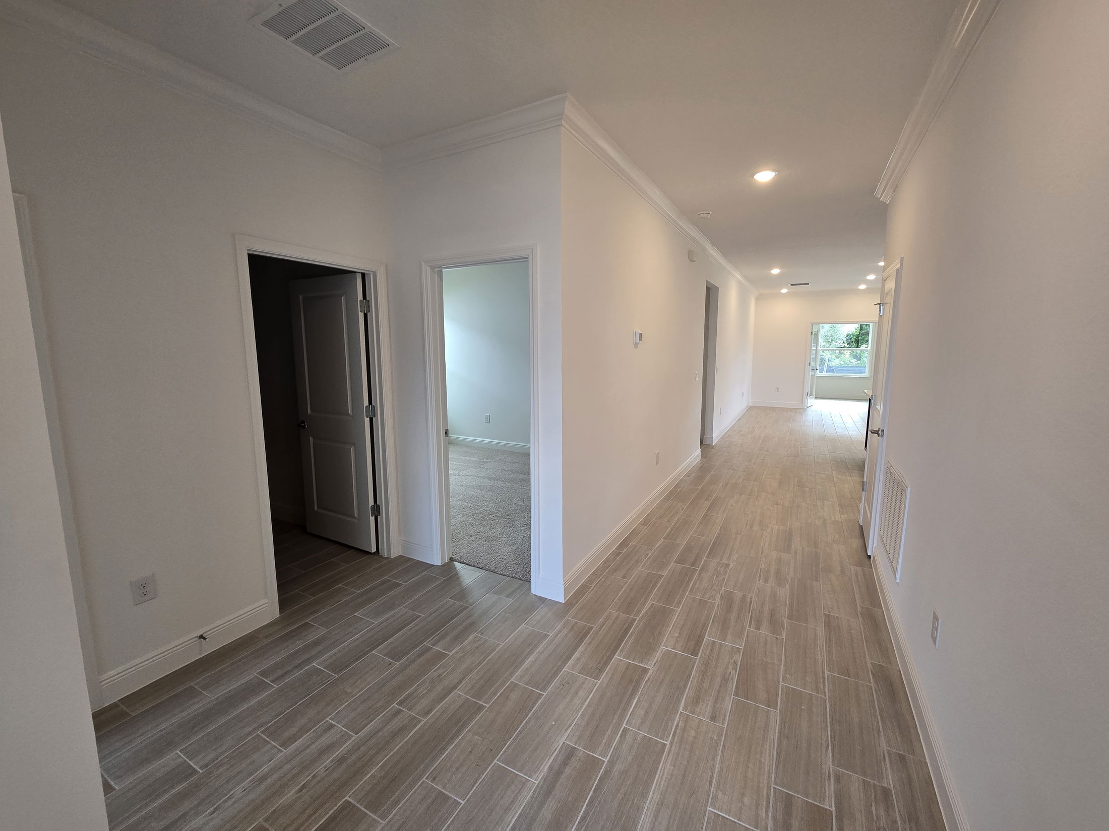 Spacious modern hallway with wooden tile flooring and multiple doorways in a bright, upscale apartment.