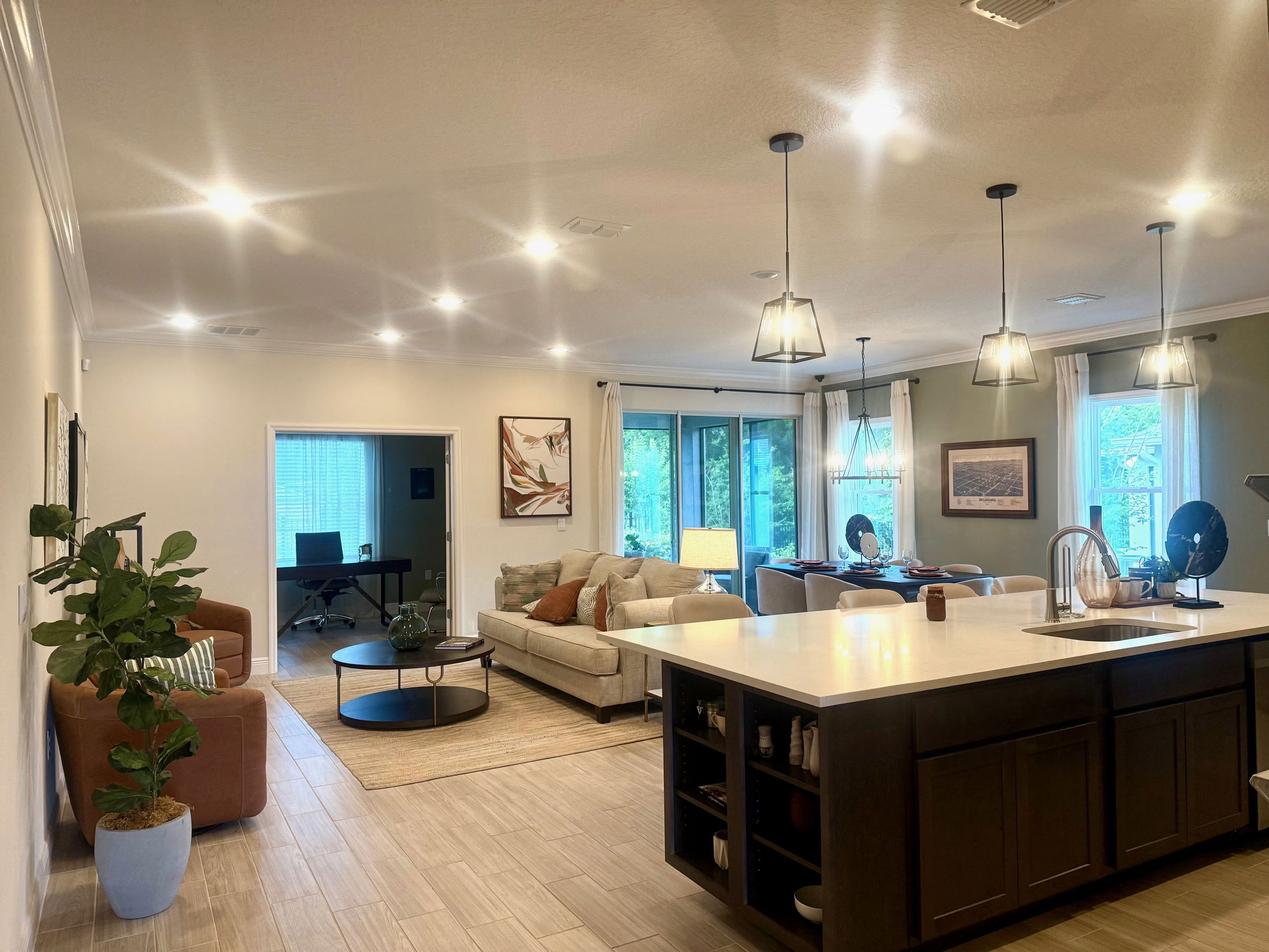 Modern open-concept living room and kitchen with stylish lighting, neutral decor, and large windows.