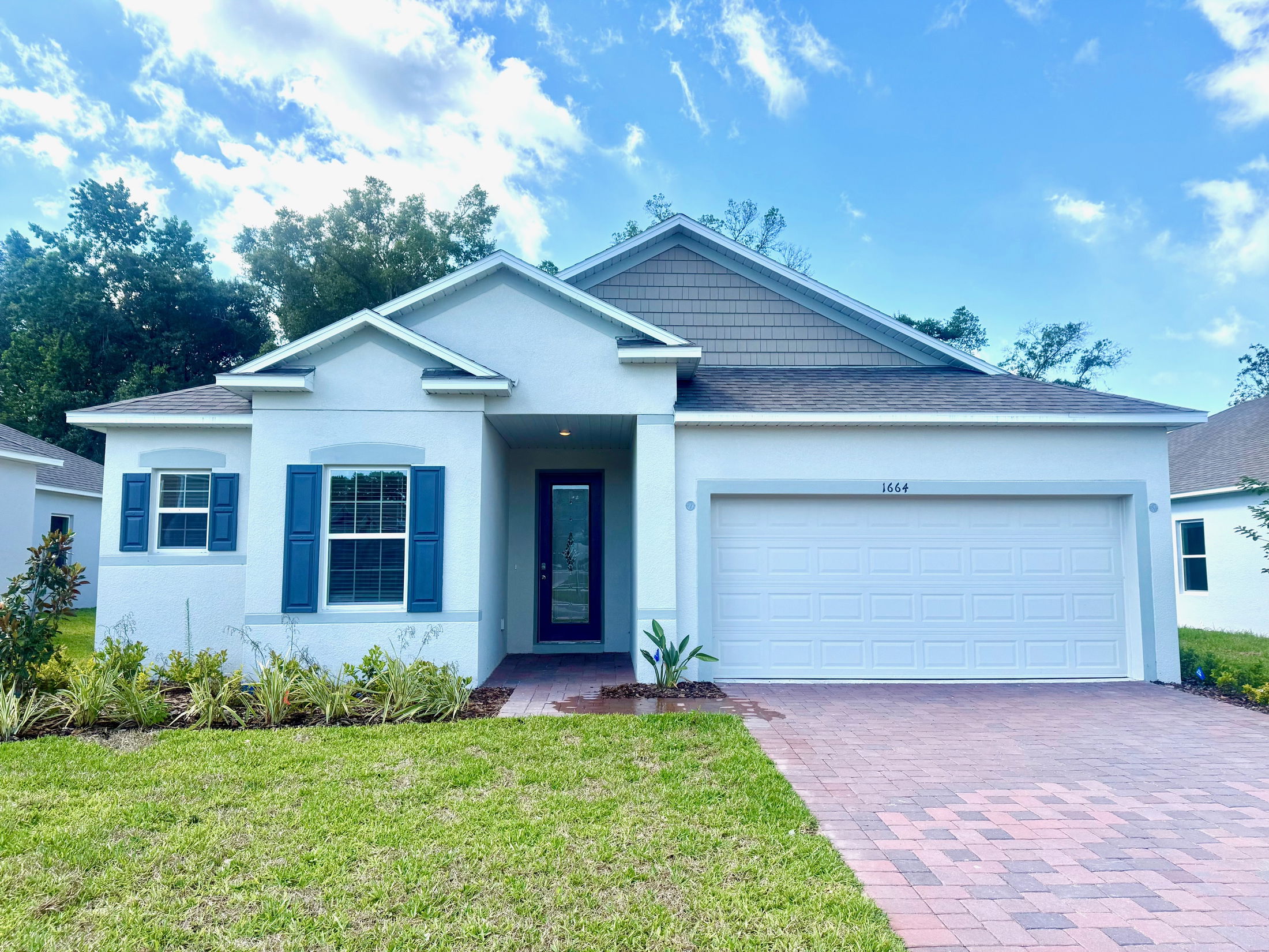 Modern suburban single-family home with blue shutters, white garage, and landscaped front yard under a clear blue sky.