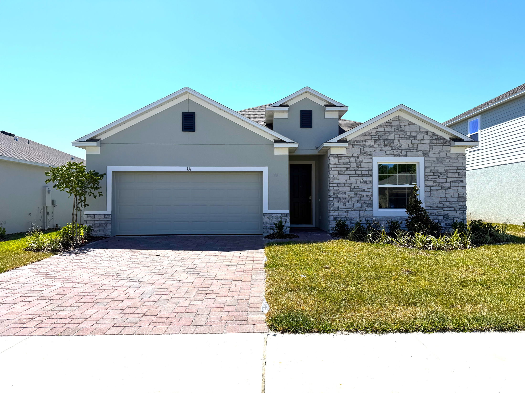 Single-story modern suburban home with gray siding, a stone facade, double garage, and a landscaped front yard.