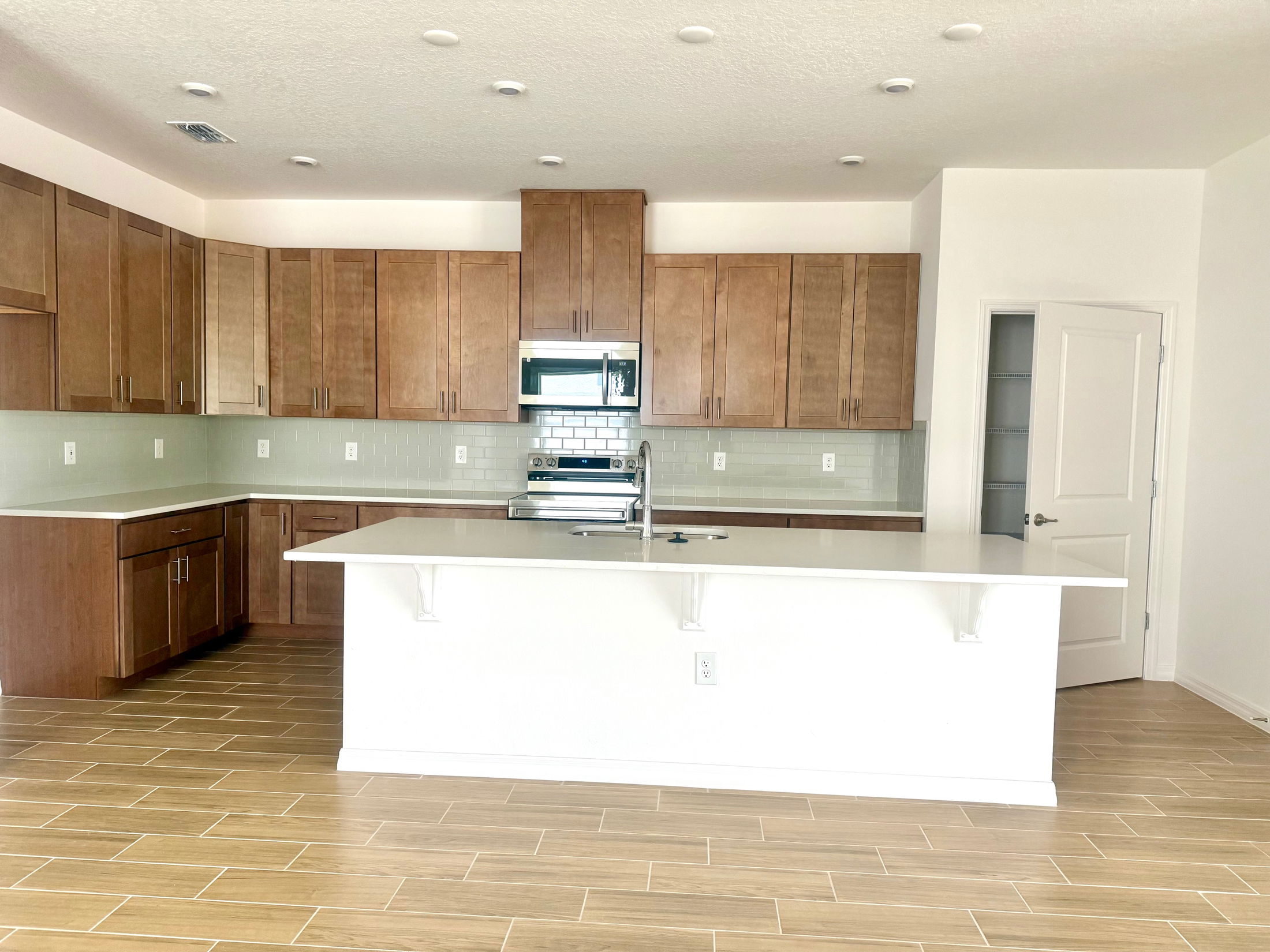 Modern kitchen with wooden cabinets, white countertops, and a tiled floor.