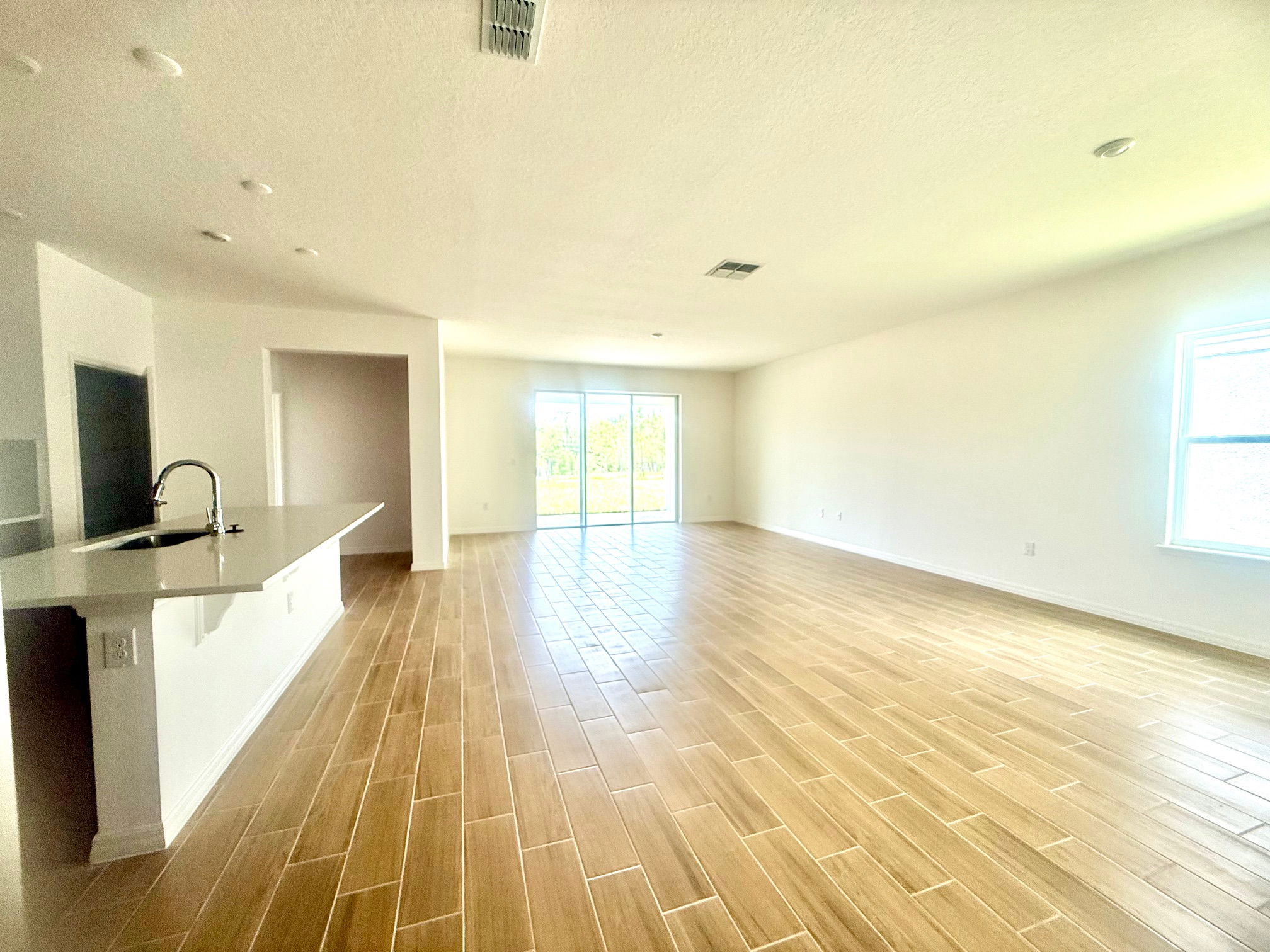 Spacious open-concept living area with wooden tile flooring, large windows, and a modern kitchen featuring a sleek countertop and sink.