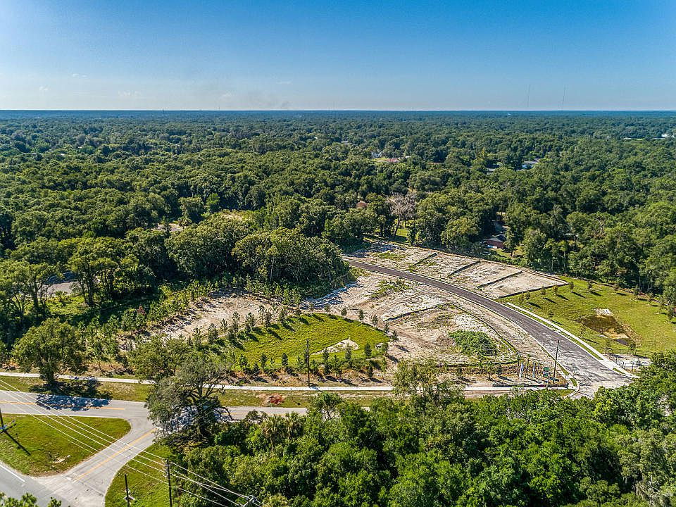Aerial view of a construction site with cleared land and surrounding forested area under clear blue skies.