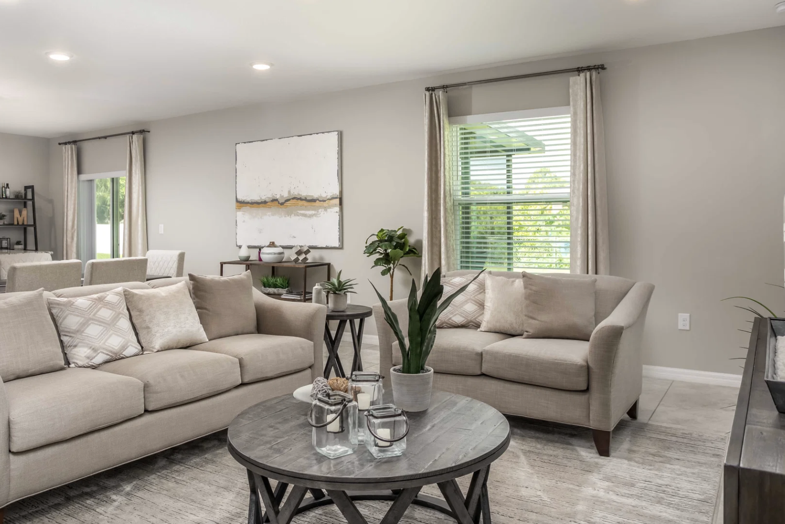 Modern living room interior featuring beige sofas, a round wooden coffee table, decorative plants, and natural light coming through the window.