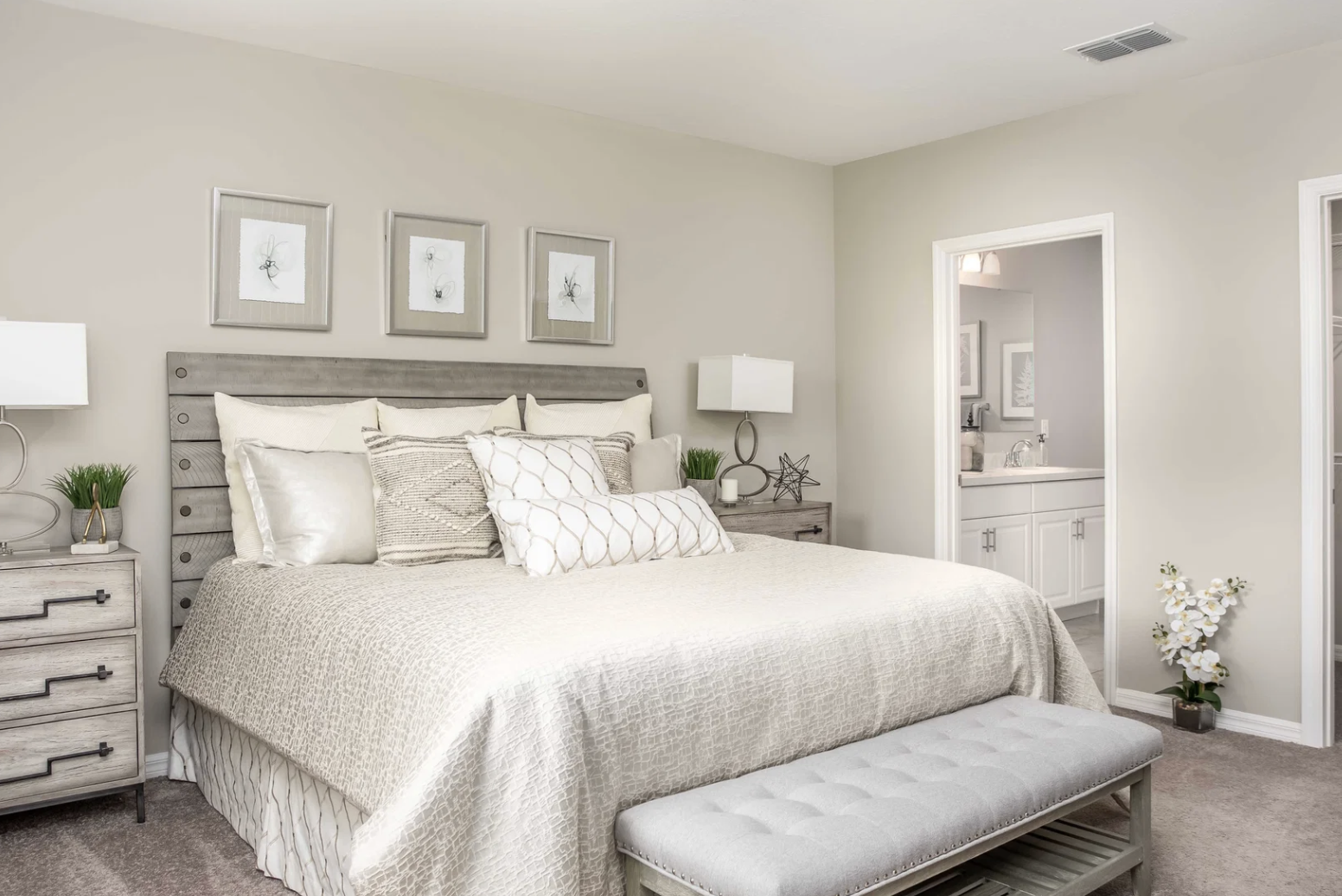 Cozy bedroom featuring a bed with decorative pillows, framed wall art, and a light gray bench at the foot.